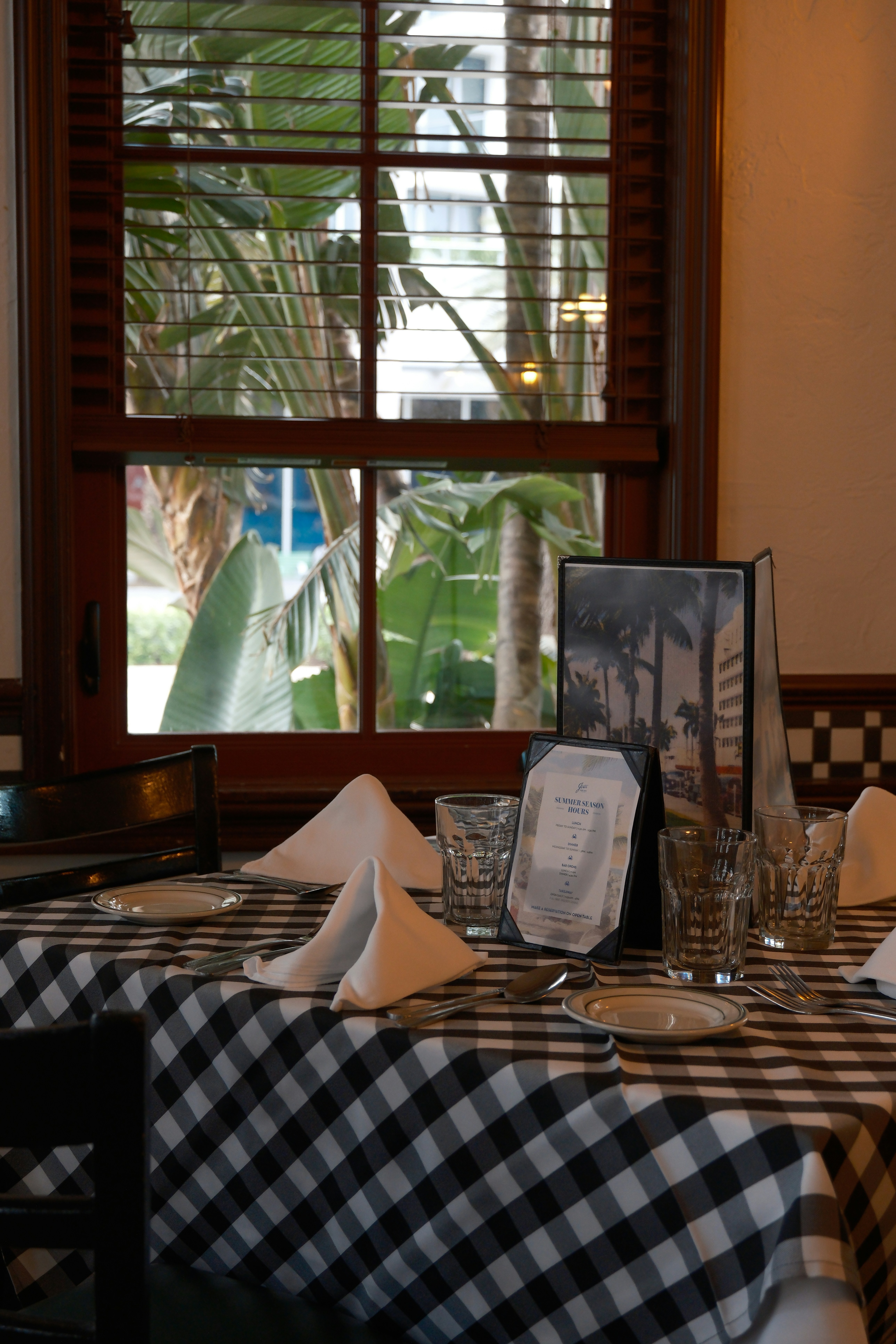 Table setting with checkered cloth and palm trees outside.
