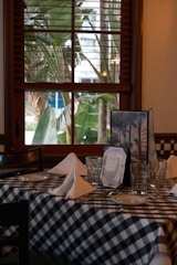 Table setting with checkered cloth and palm trees outside.