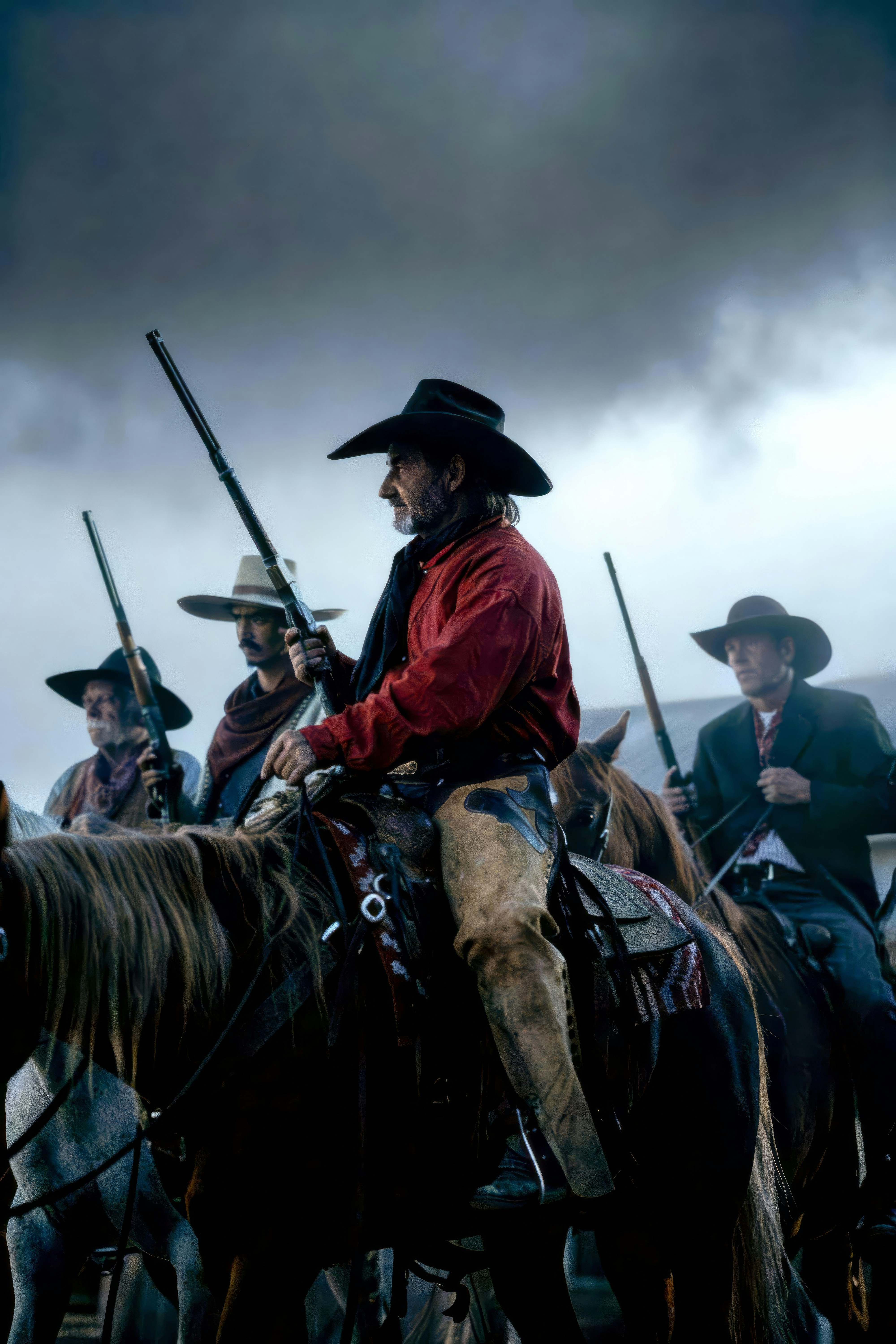 Cowboys on horseback with rifles under cloudy sky.