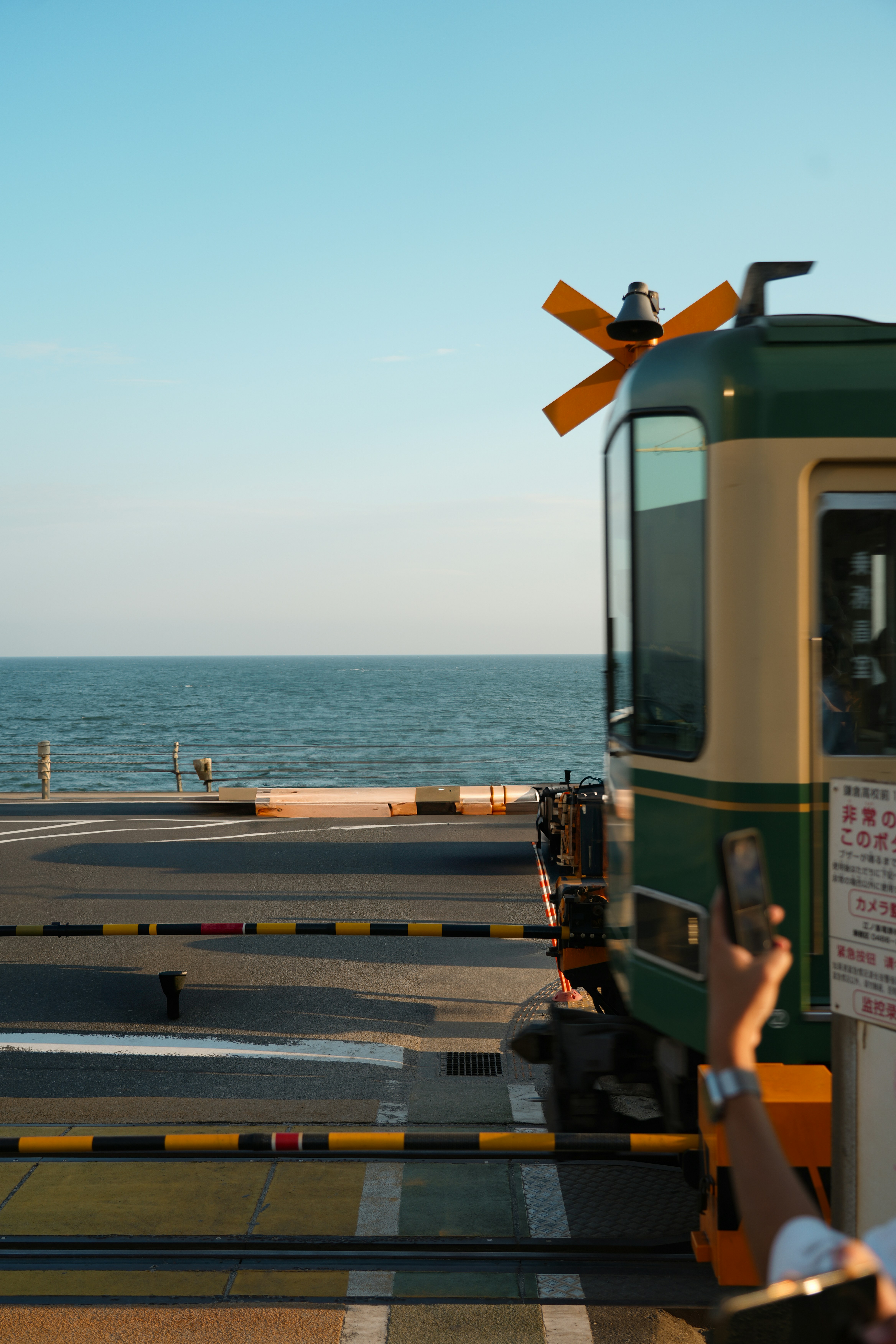 Train crossing tracks by the ocean with person taking photo.