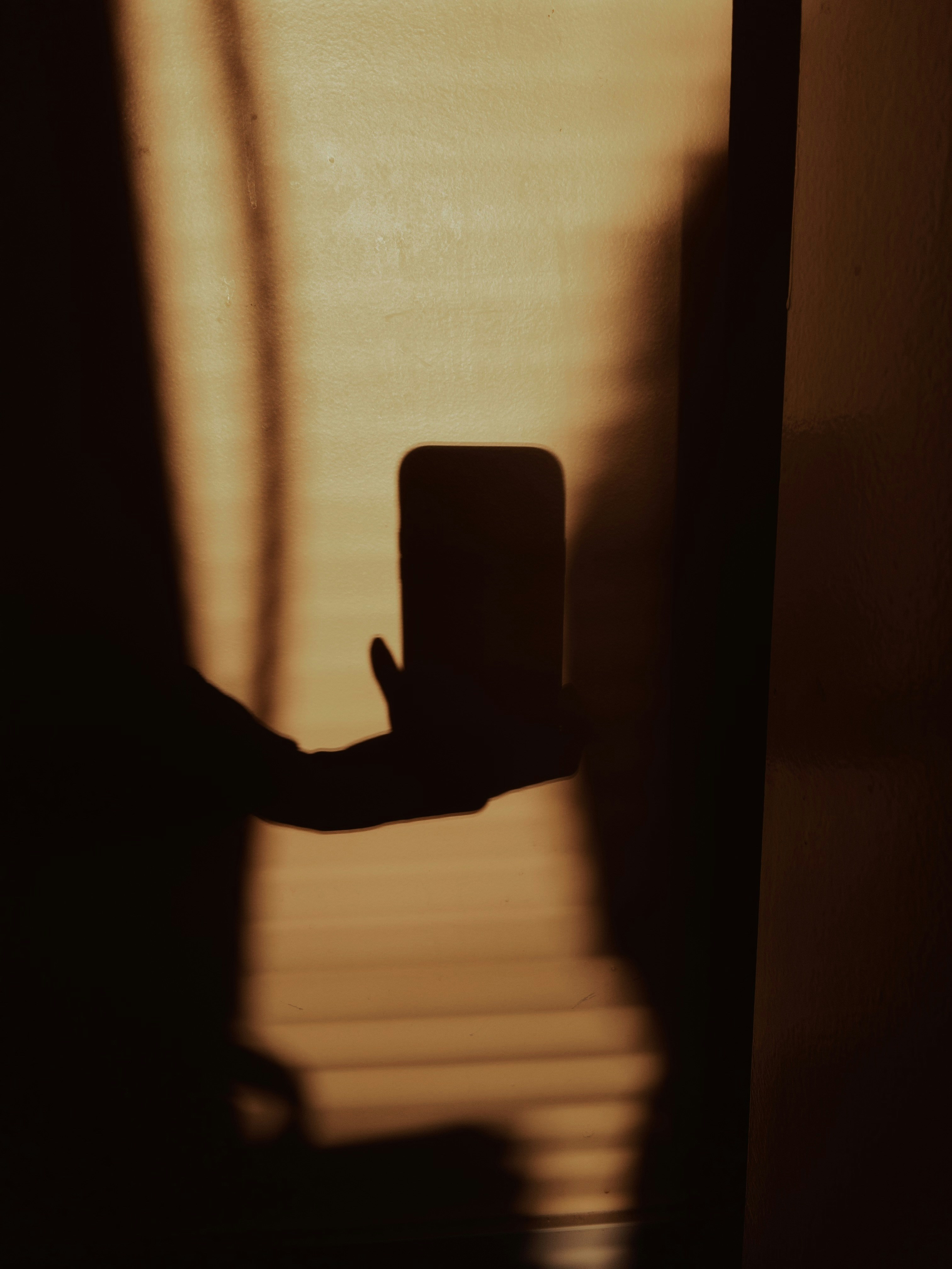 Schatten einer Hand, die ein Telefon gegen Jalousien hält.