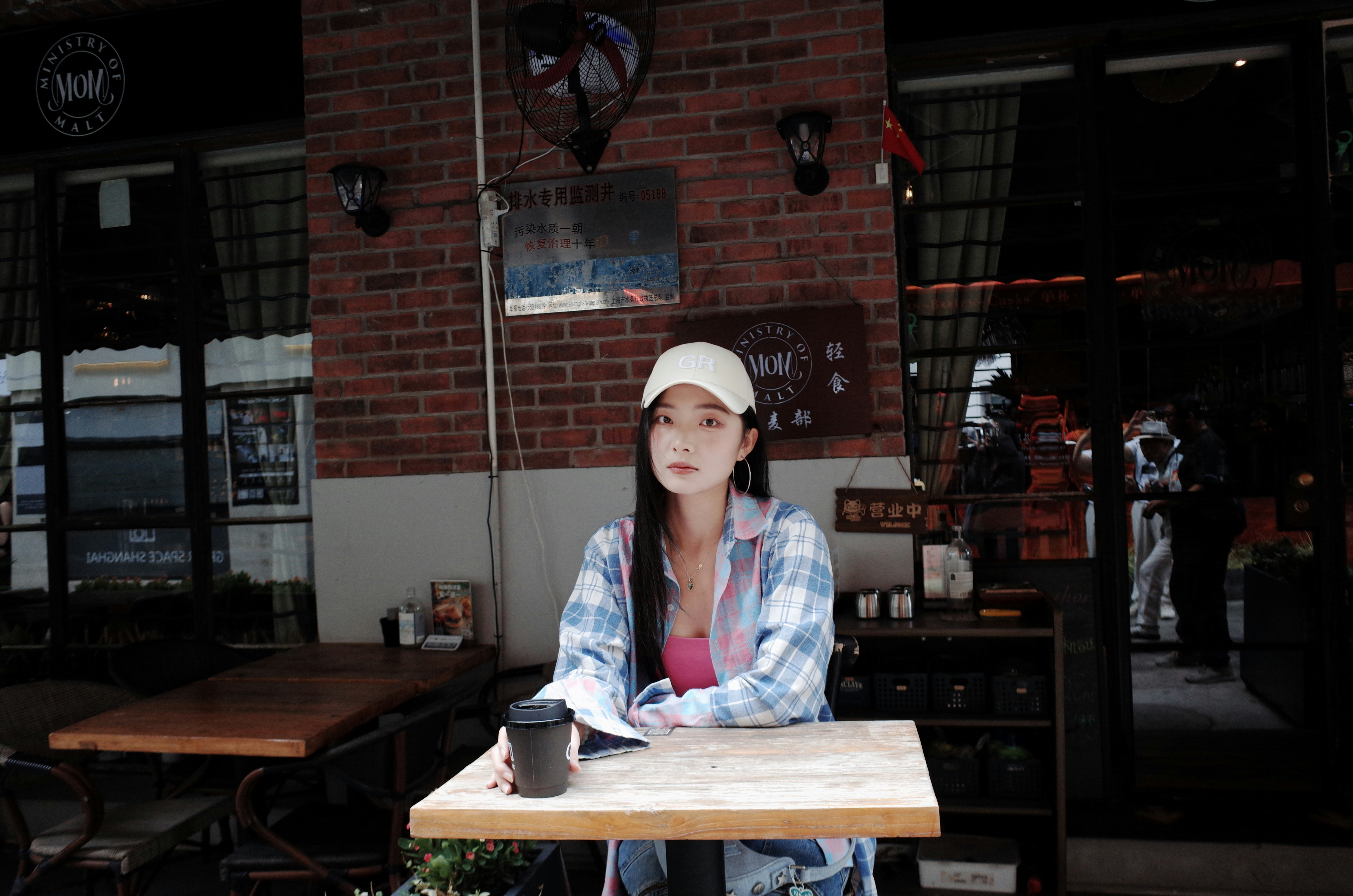 Woman in cap sits at cafe table with coffee