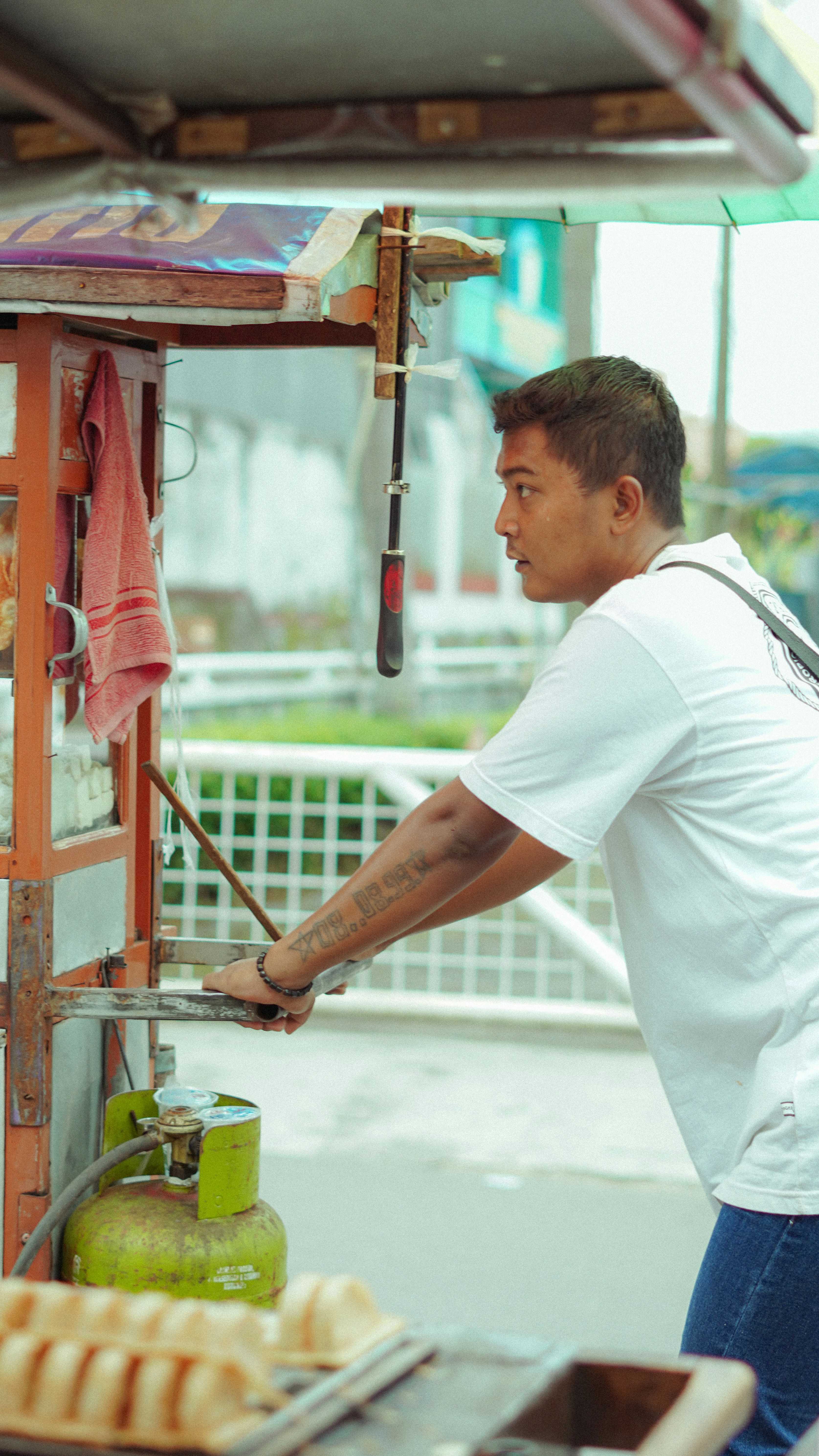 Man operating a food cart with gas cylinder.