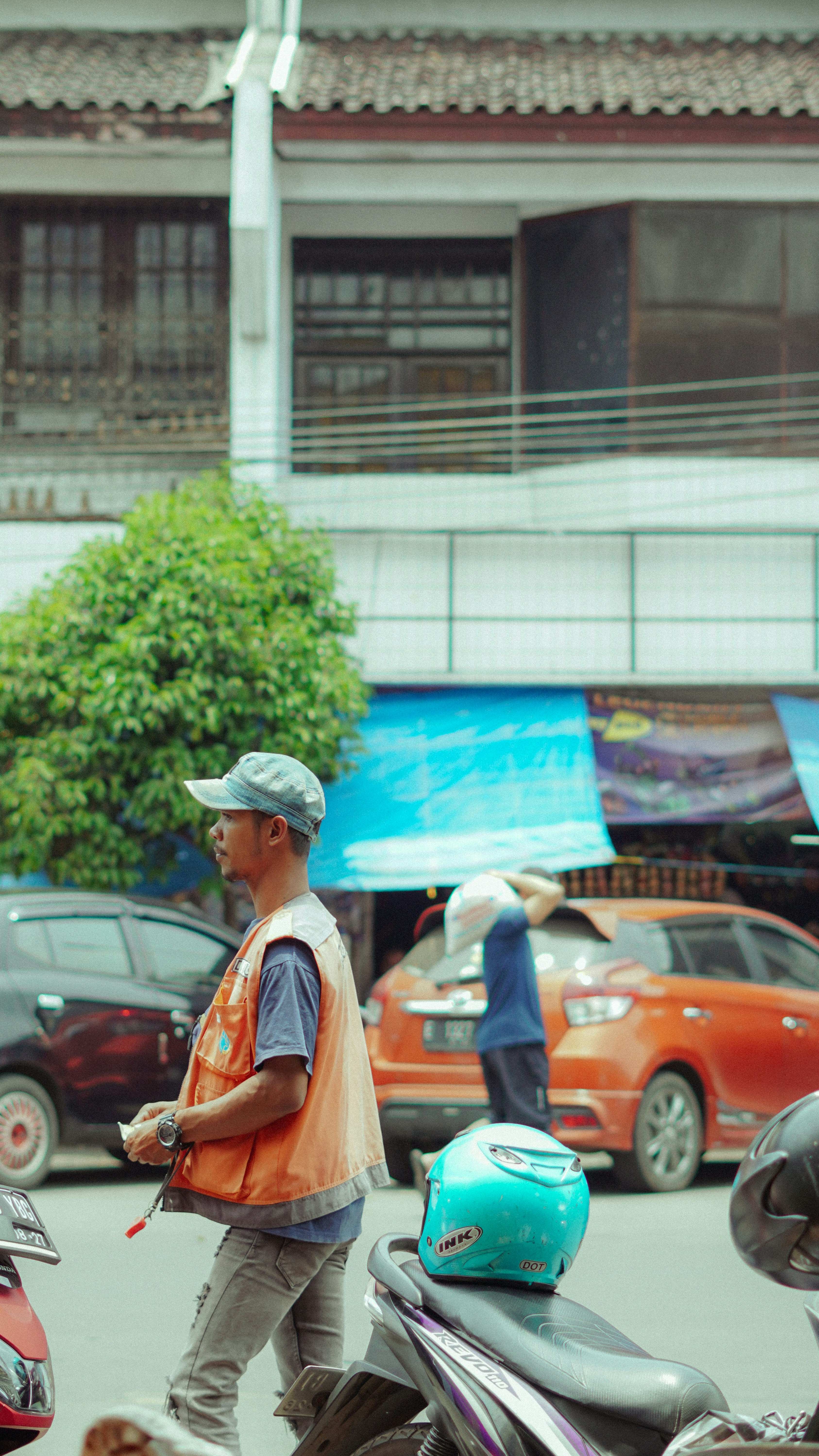 Man in orange vest on street with cars and motorcycle.