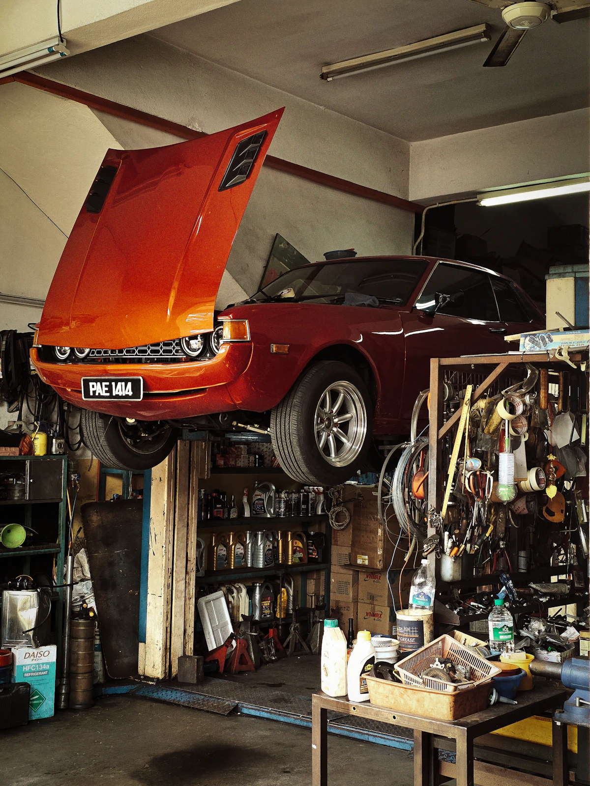 Une voiture levée sur un pont élévateur dans un atelier de garage, capot ouvert et outils rangés au mur