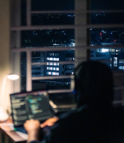 Person working on laptop at night with city view.