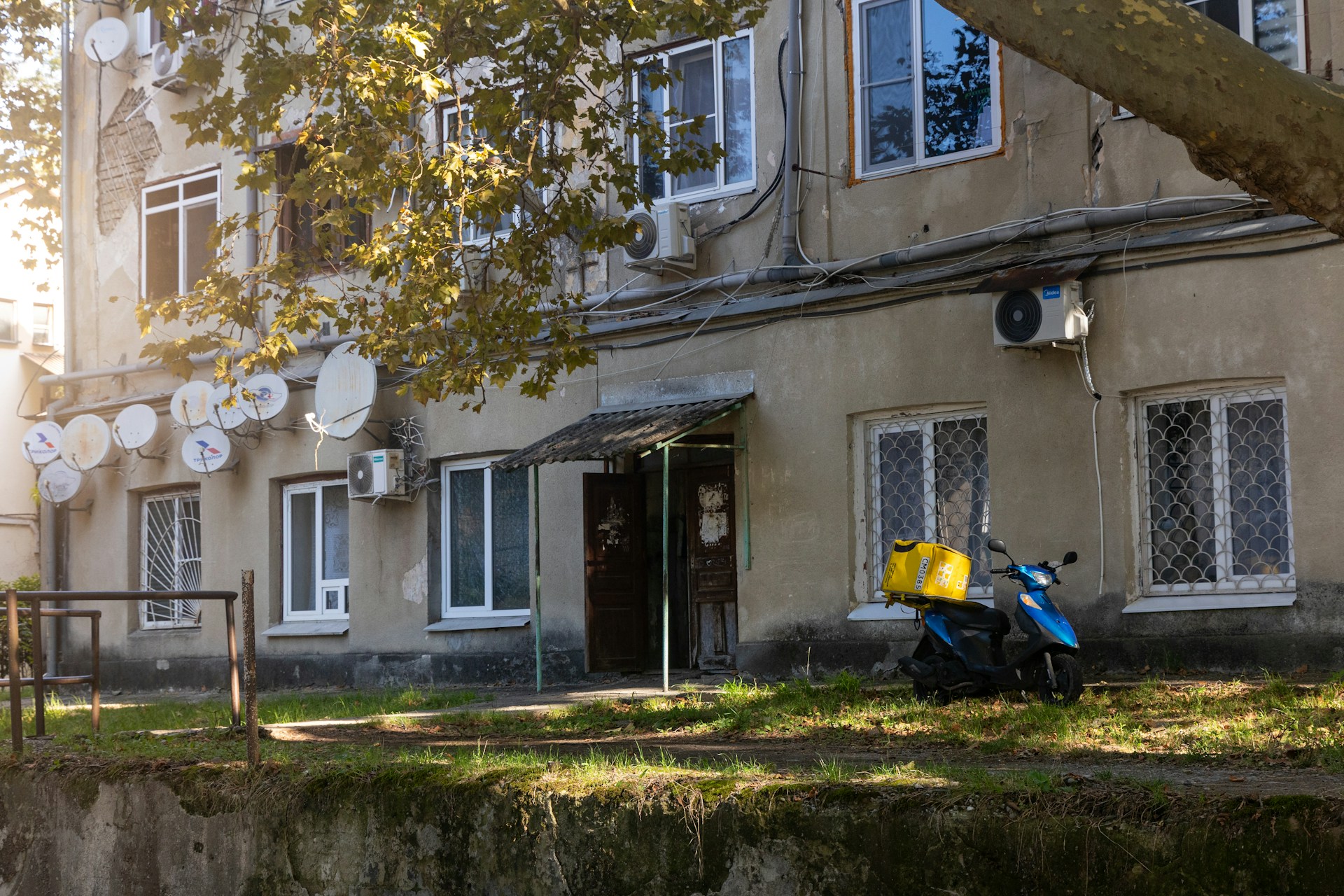 A blue scooter with a yellow box parked outside building.