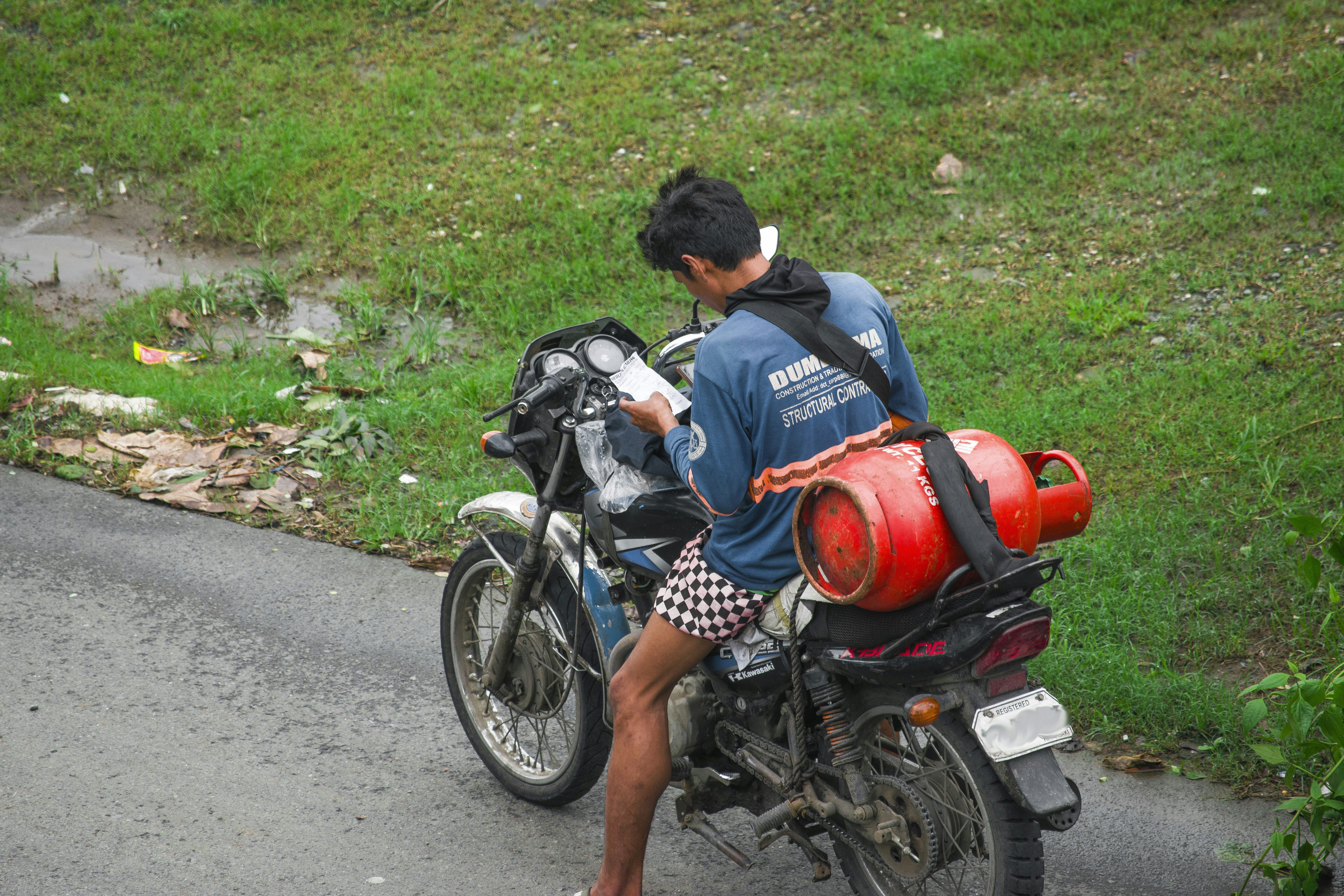 Man riding motorcycle with gas cylinder on back.