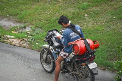 Man riding motorcycle with gas cylinder on back.