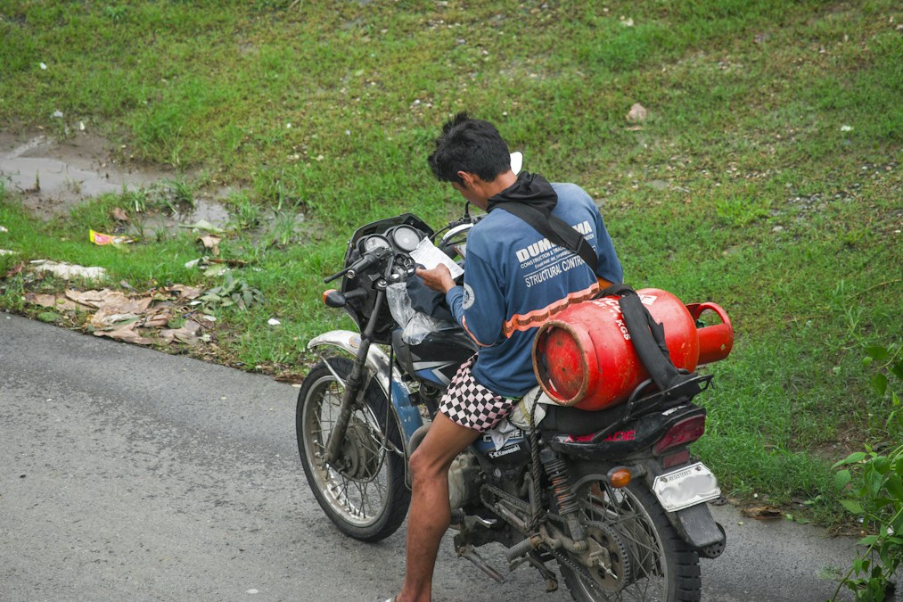 Un livreur à moto transporte une bouteille de gaz rouge sanglée à l’arrière de son siège