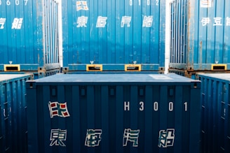 Stacked blue shipping containers with japanese text.