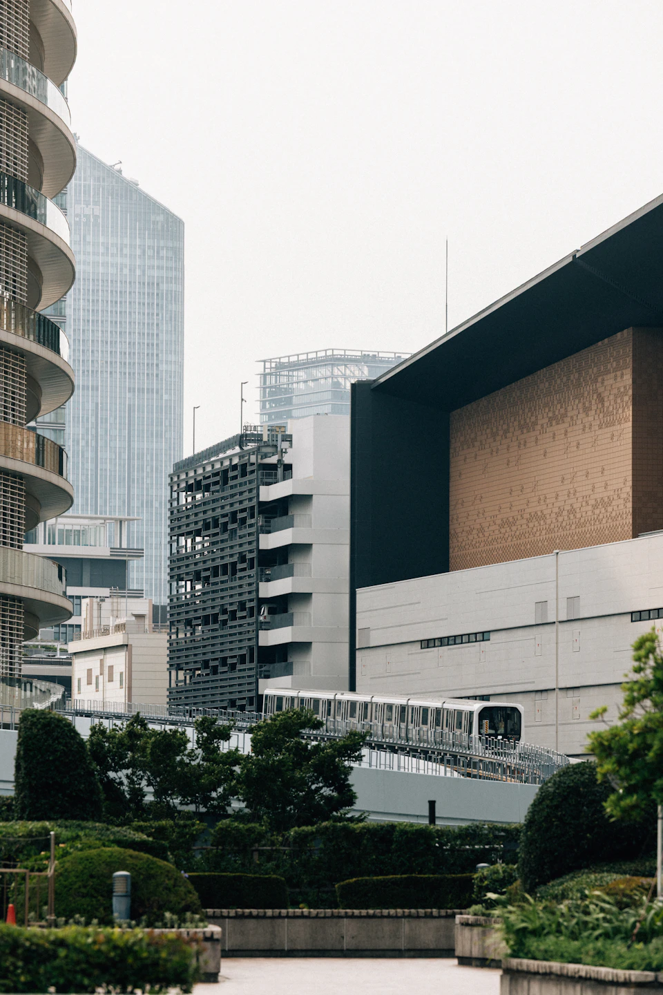 Modern glass building with curved facade reflects overcast sky amidst lush green surroundings nearby