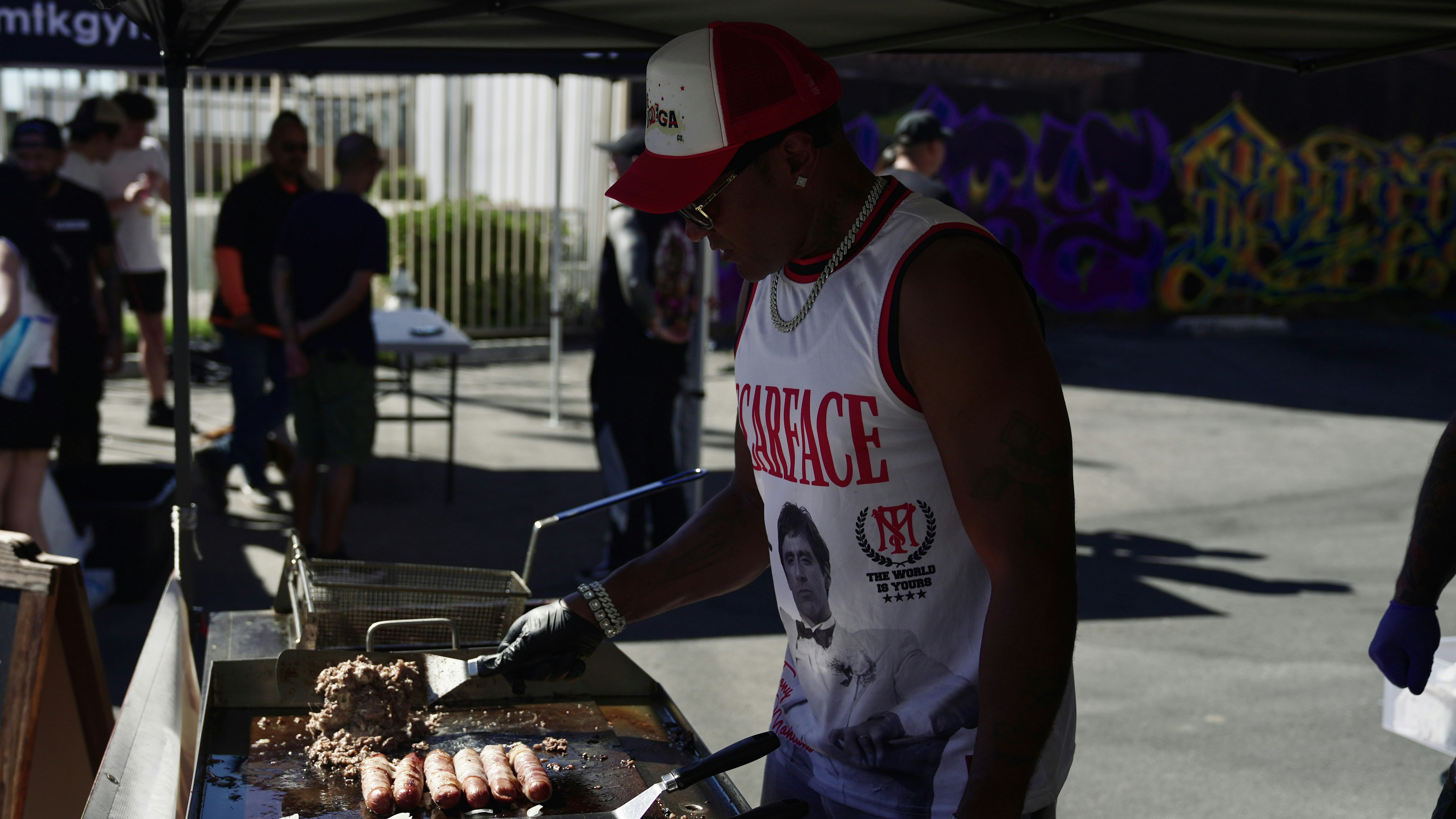 Man grilling sausages and burgers outdoors at a food stand.