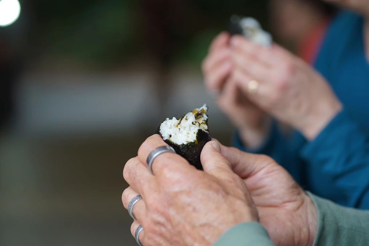 A traveler holding a half-eaten onigiri rice ball wrapped in seaweed at Meiji Shrine, Tokyo