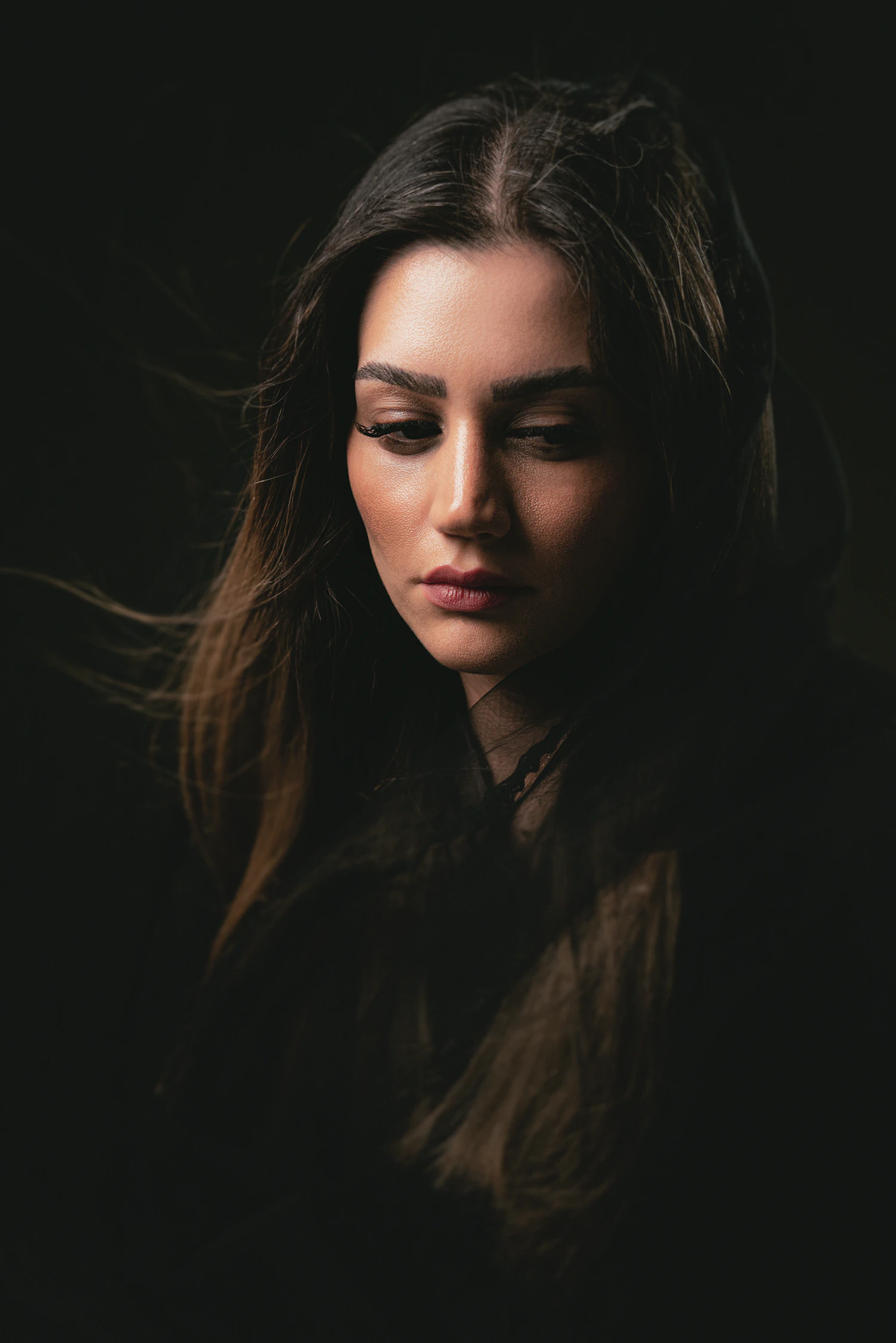 Long, glossy brown hair falling over one shoulder as a woman looks down in warm low light
