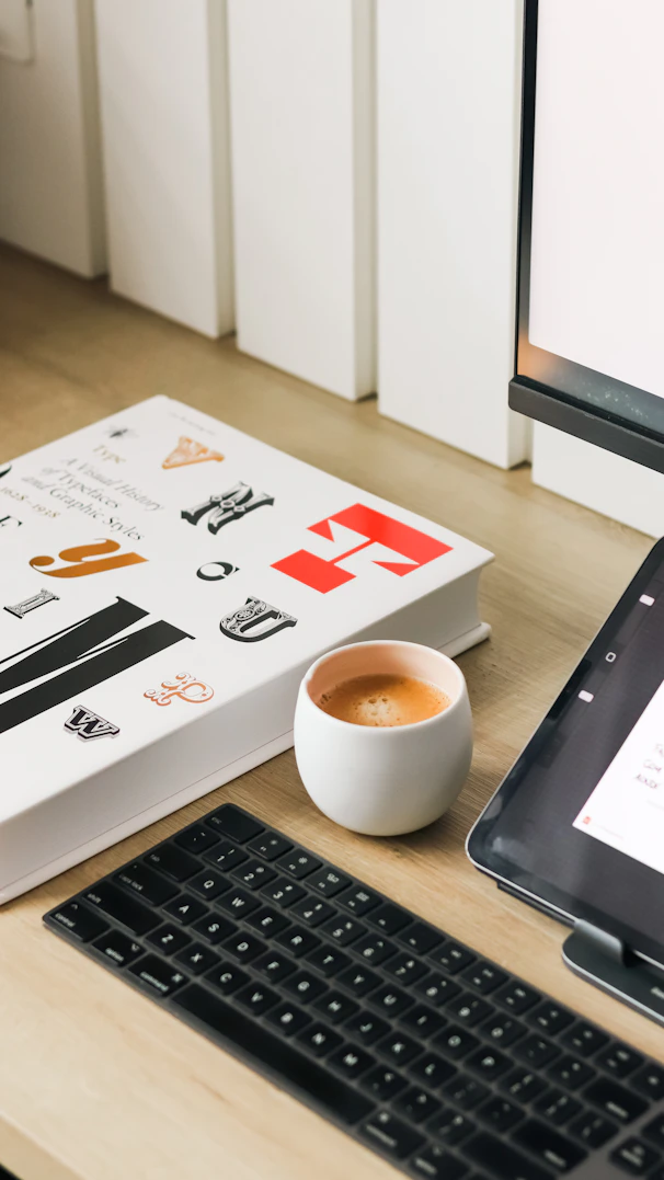 A book, coffee, and keyboard on a desk.