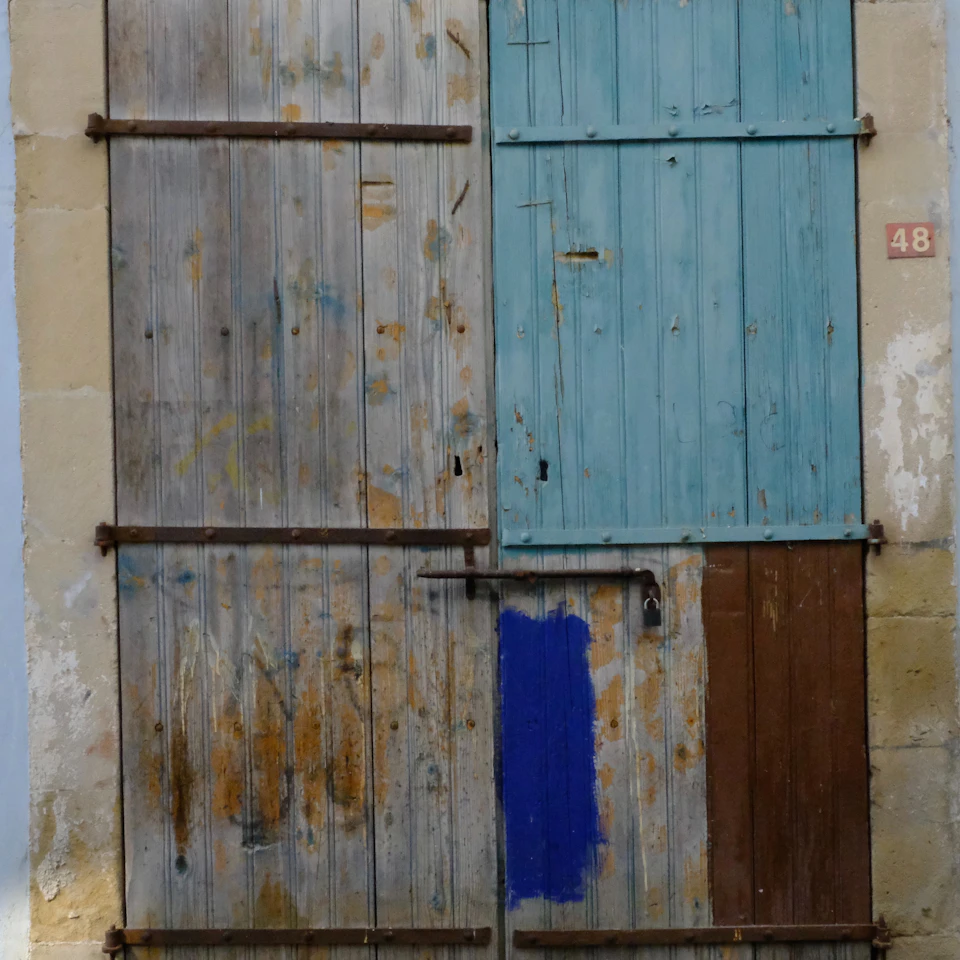 Weathered wooden door with three panels painted different colors on a stone wall