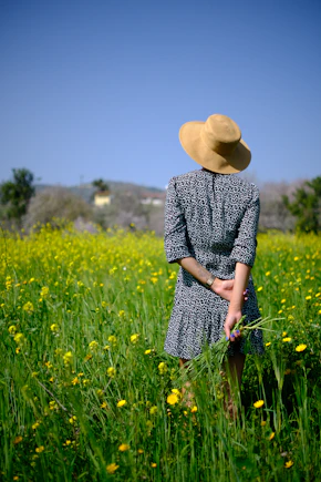 Woman in hat stands in a field of yellow flowers.