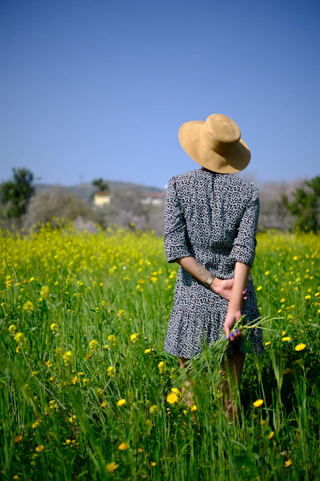 Woman in hat stands in a field of yellow flowers.