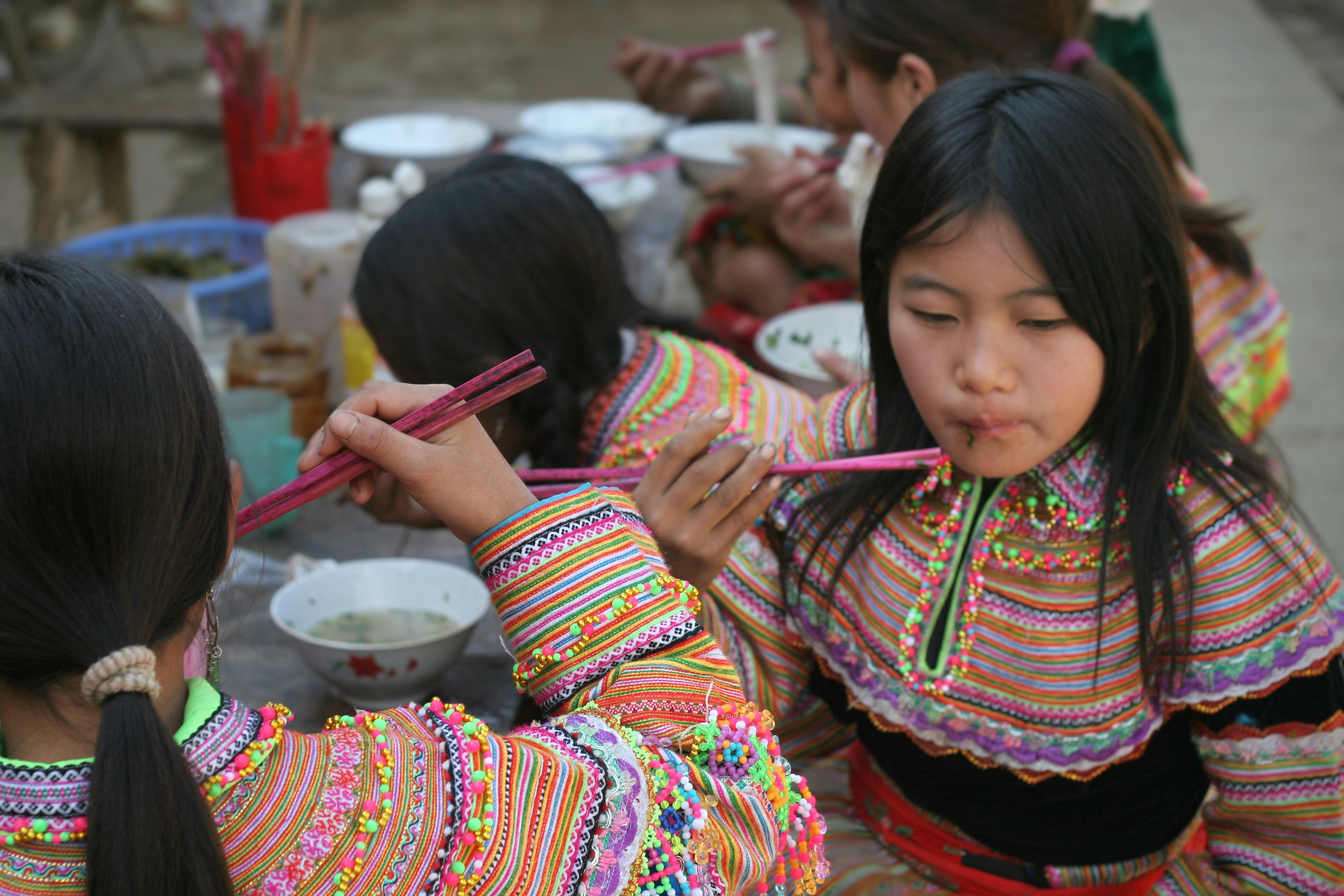 Young girls eating with chopsticks at a table.