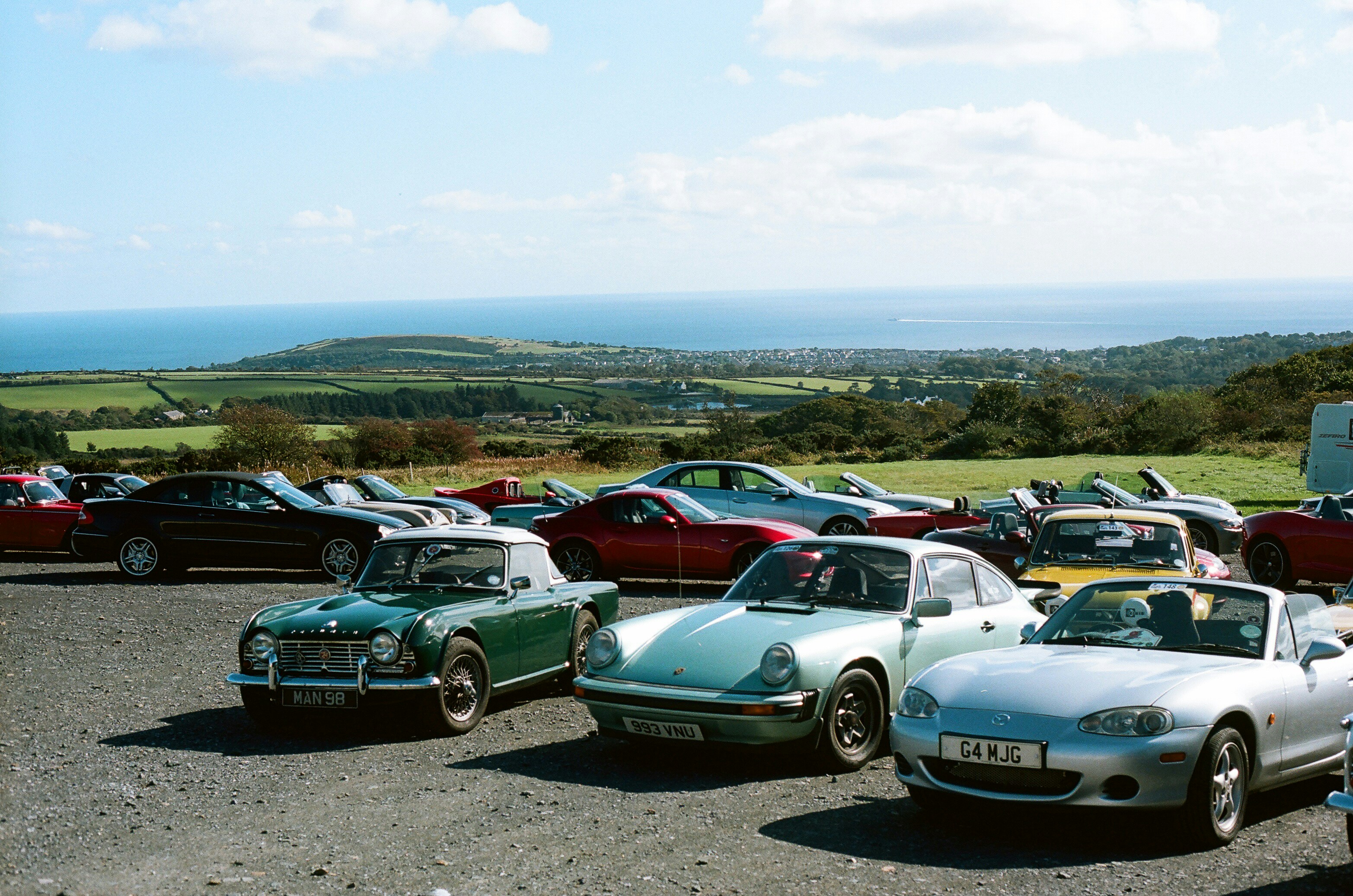 Classic and modern sports cars parked overlooking a coastal landscape.