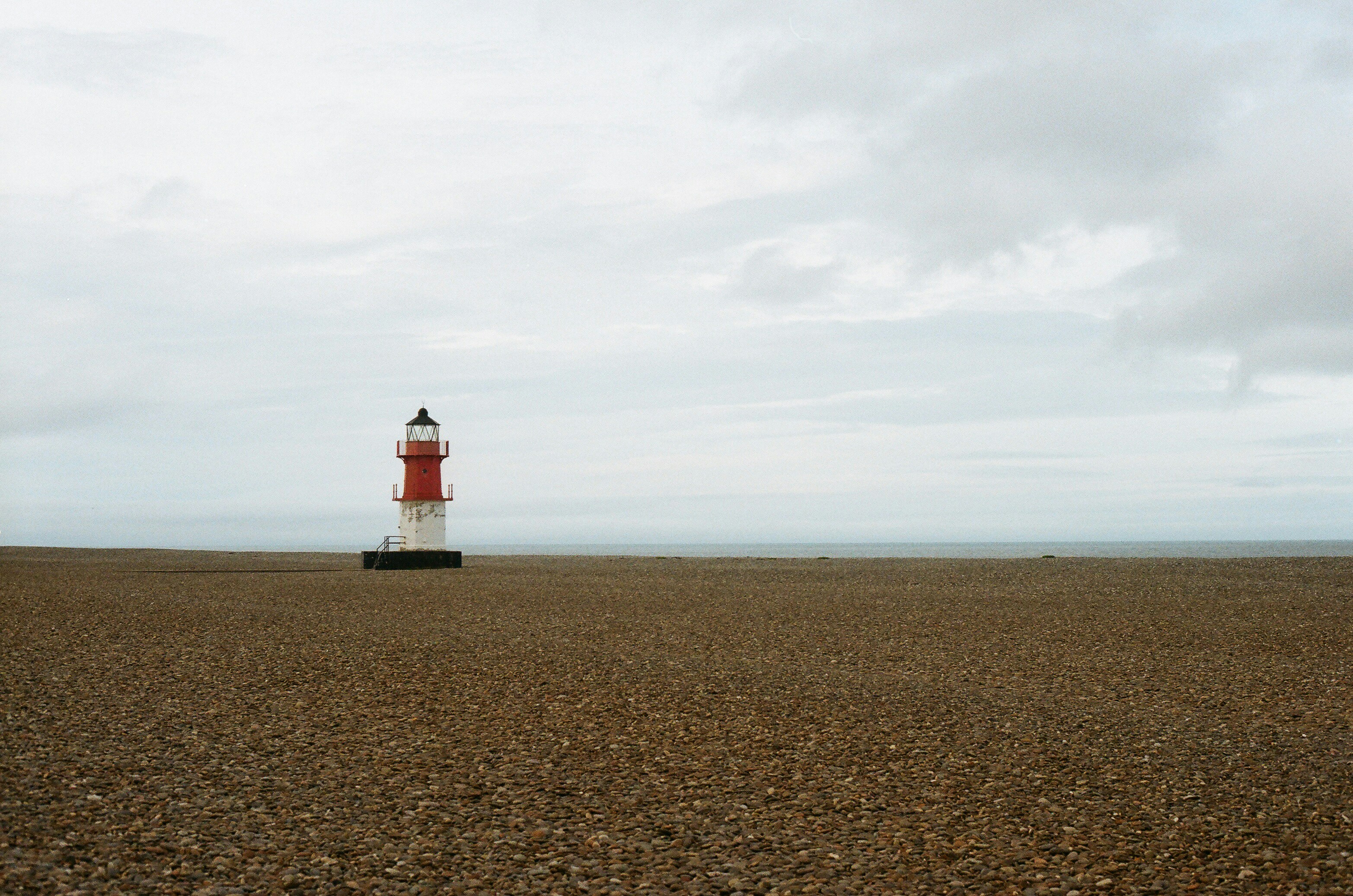 Red and white lighthouse on a pebble beach.