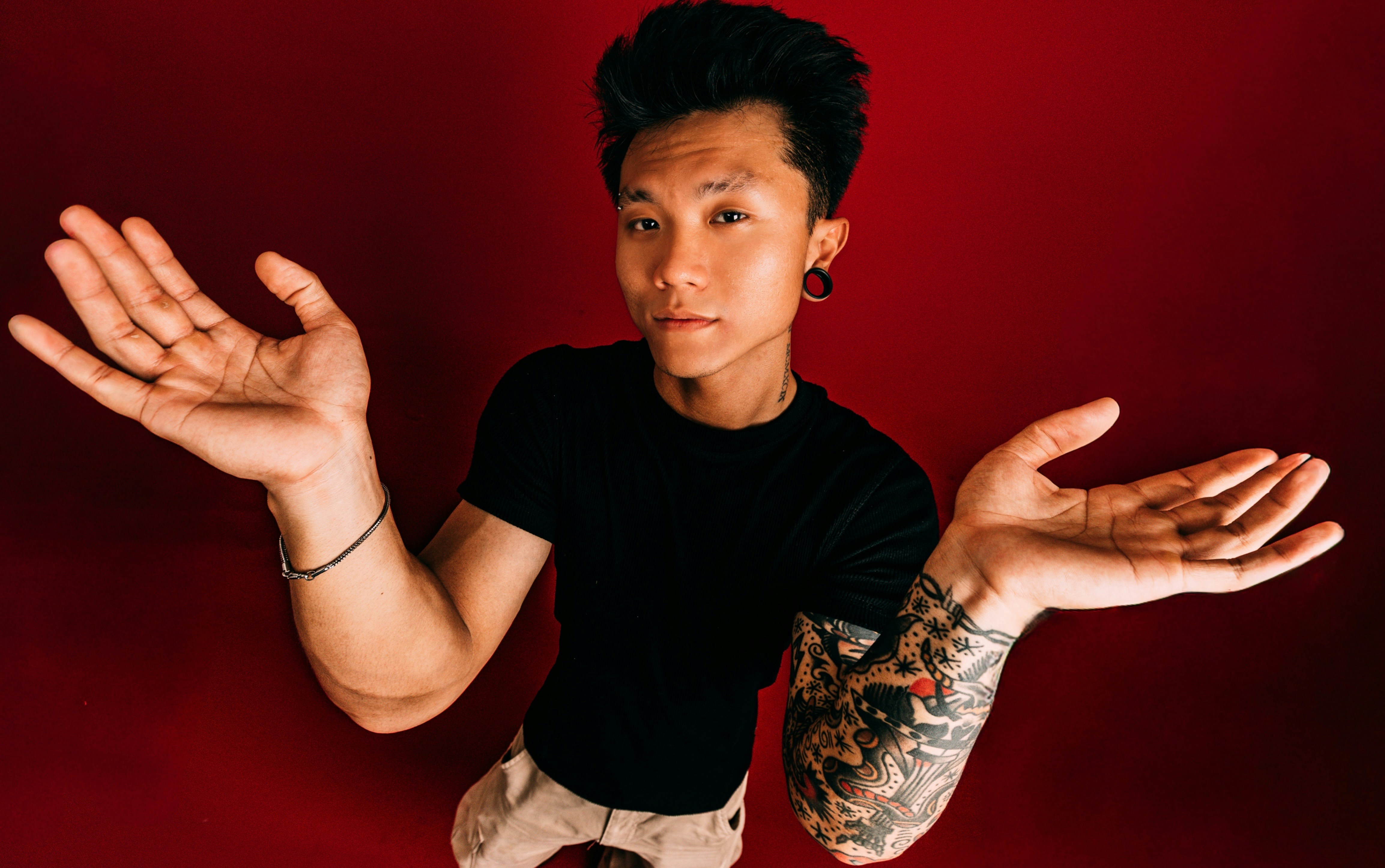 Man with tattoos shrugs with hands raised.