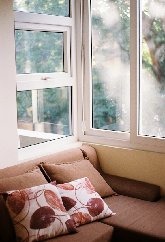 Brown sofa with patterned pillows near a window.
