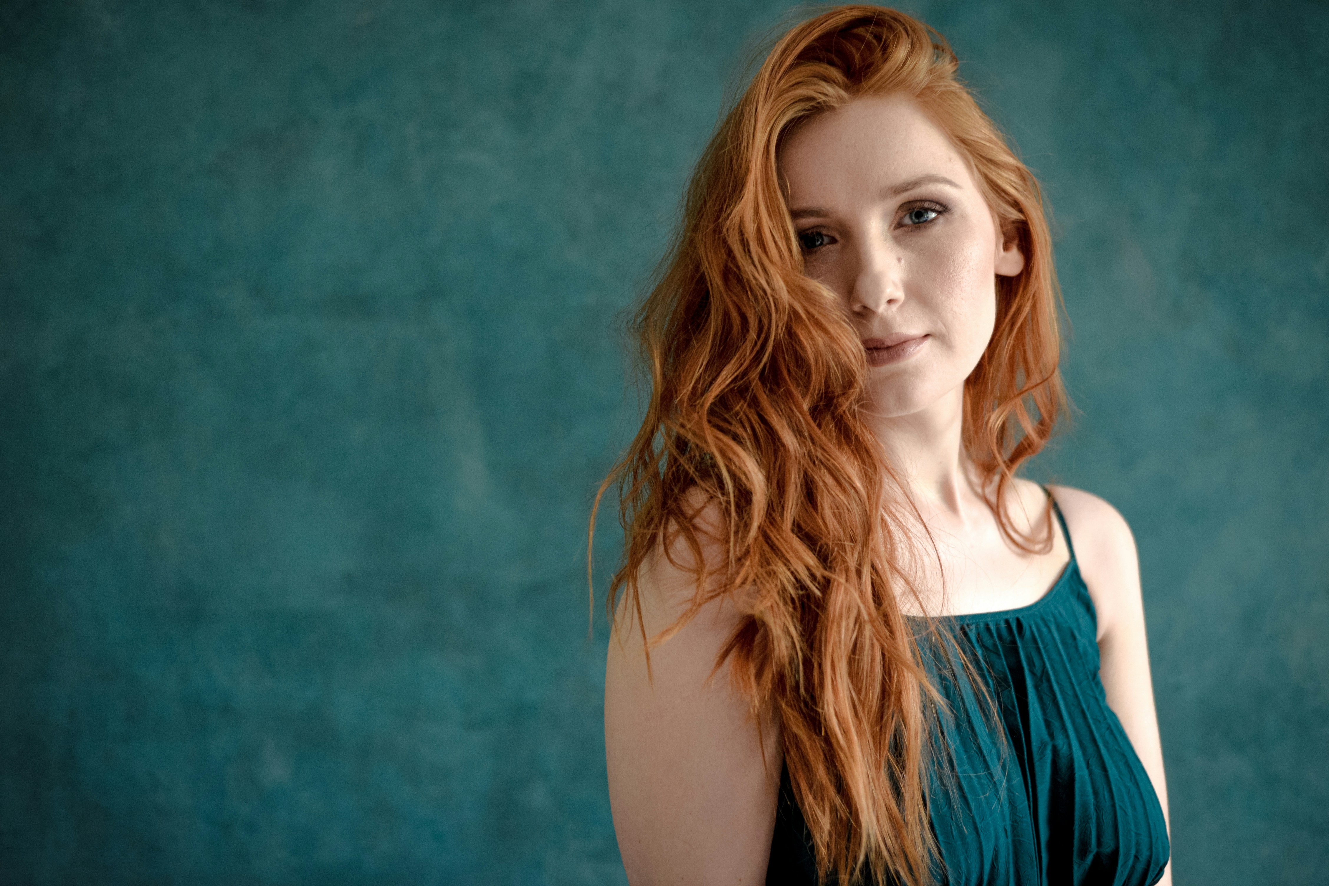 Young woman with long red hair against teal backdrop