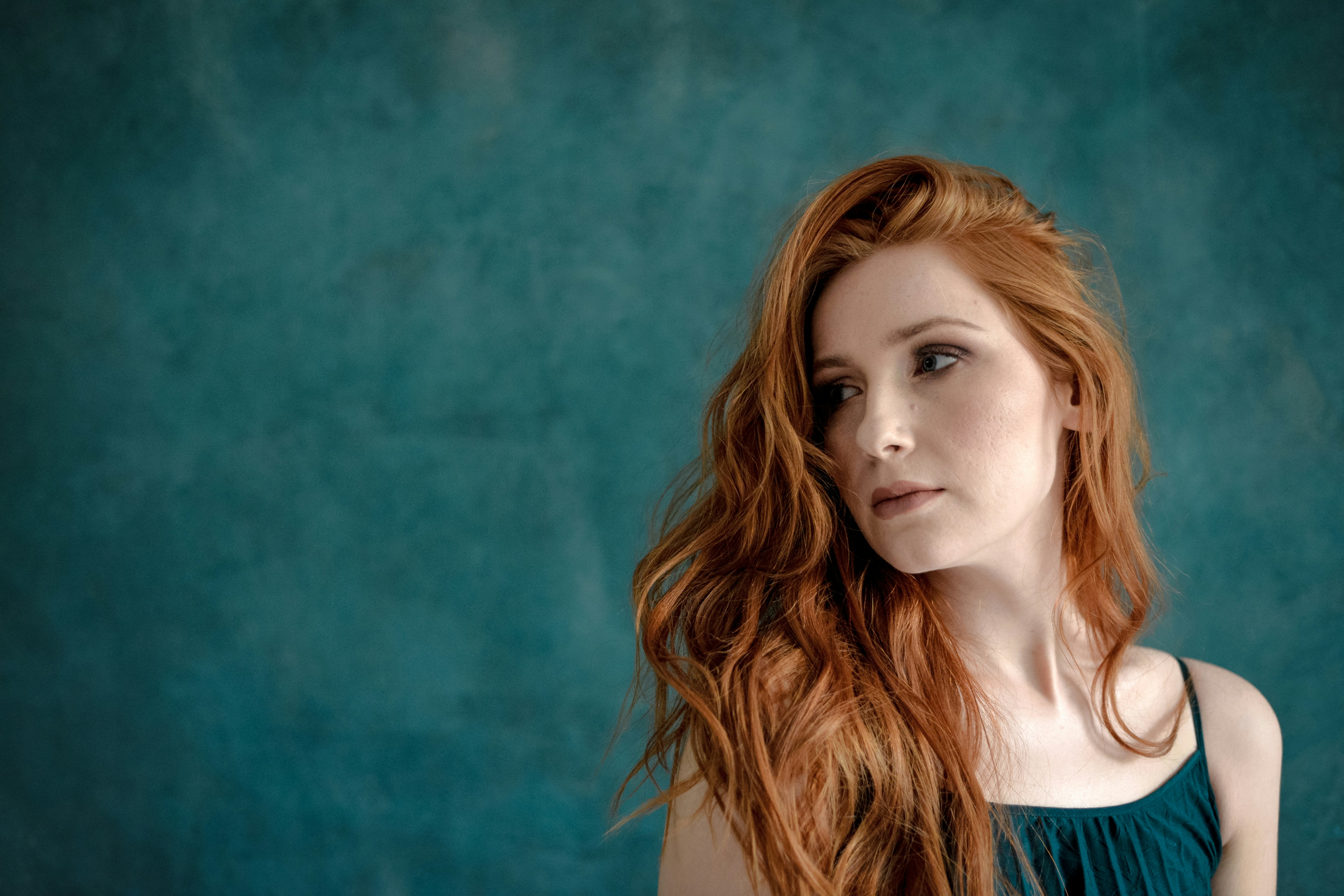 Young woman with long red hair against teal background