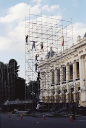 Workers climb scaffolding around a building facade.