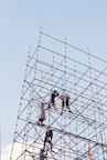 Workers assemble scaffolding against a clear blue sky.