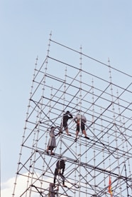 Workers assemble scaffolding against a clear blue sky.