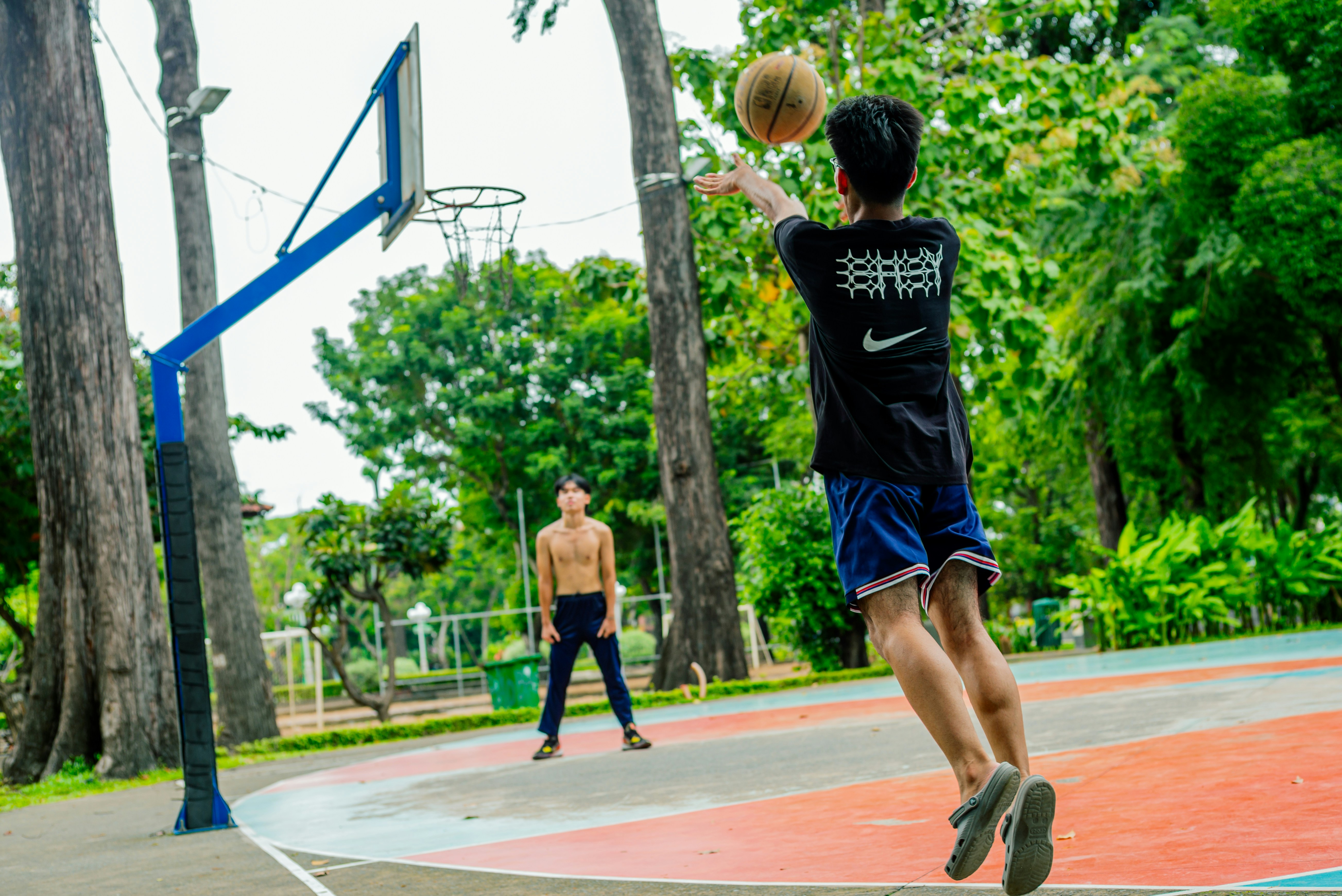 Two young men playing basketball on an outdoor court.