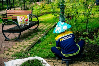 Gardener wearing conical hat tending to plants in park.