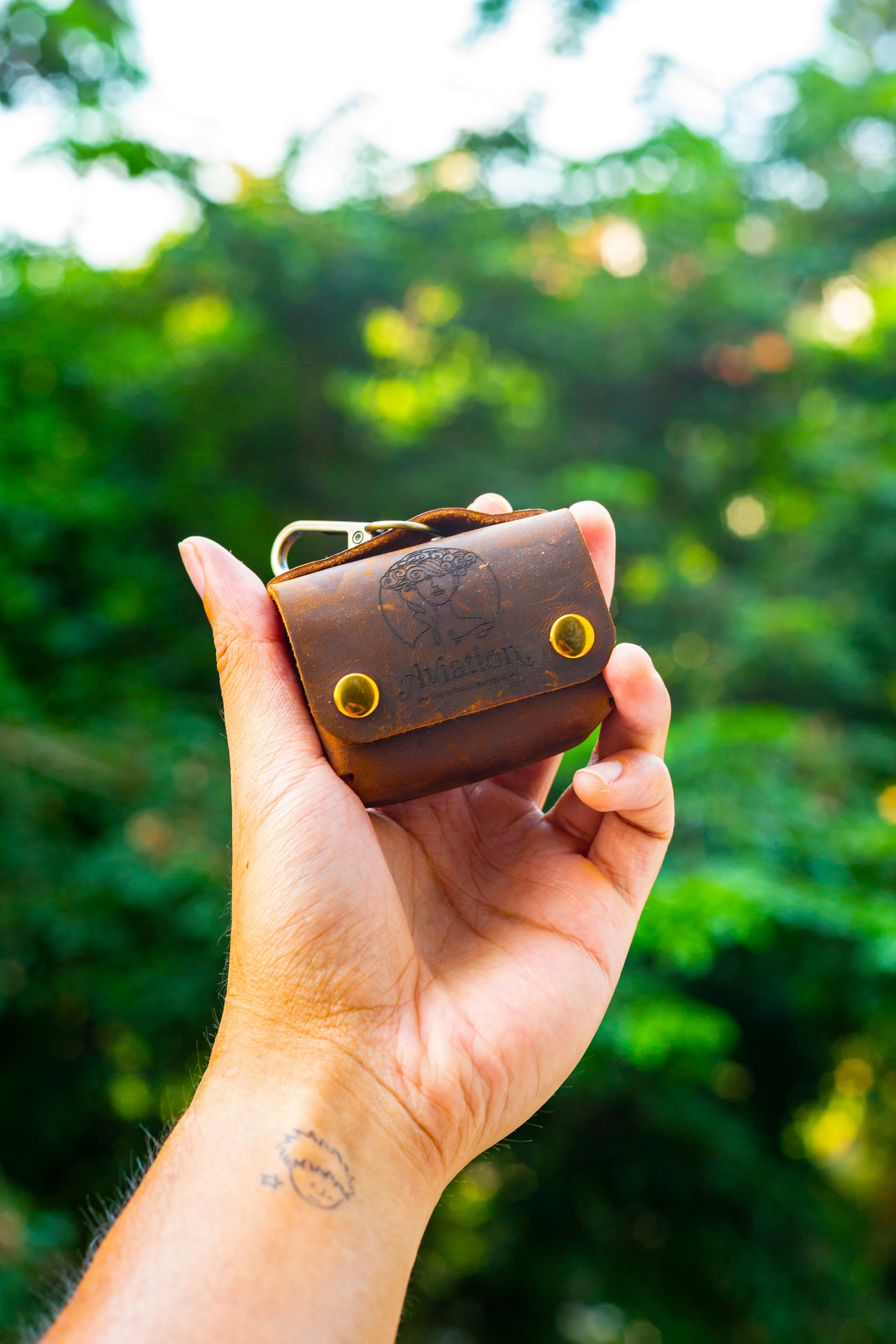 Hand holding small brown leather pouch with keychain