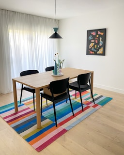 Dining table with chairs and colorful striped rug.
