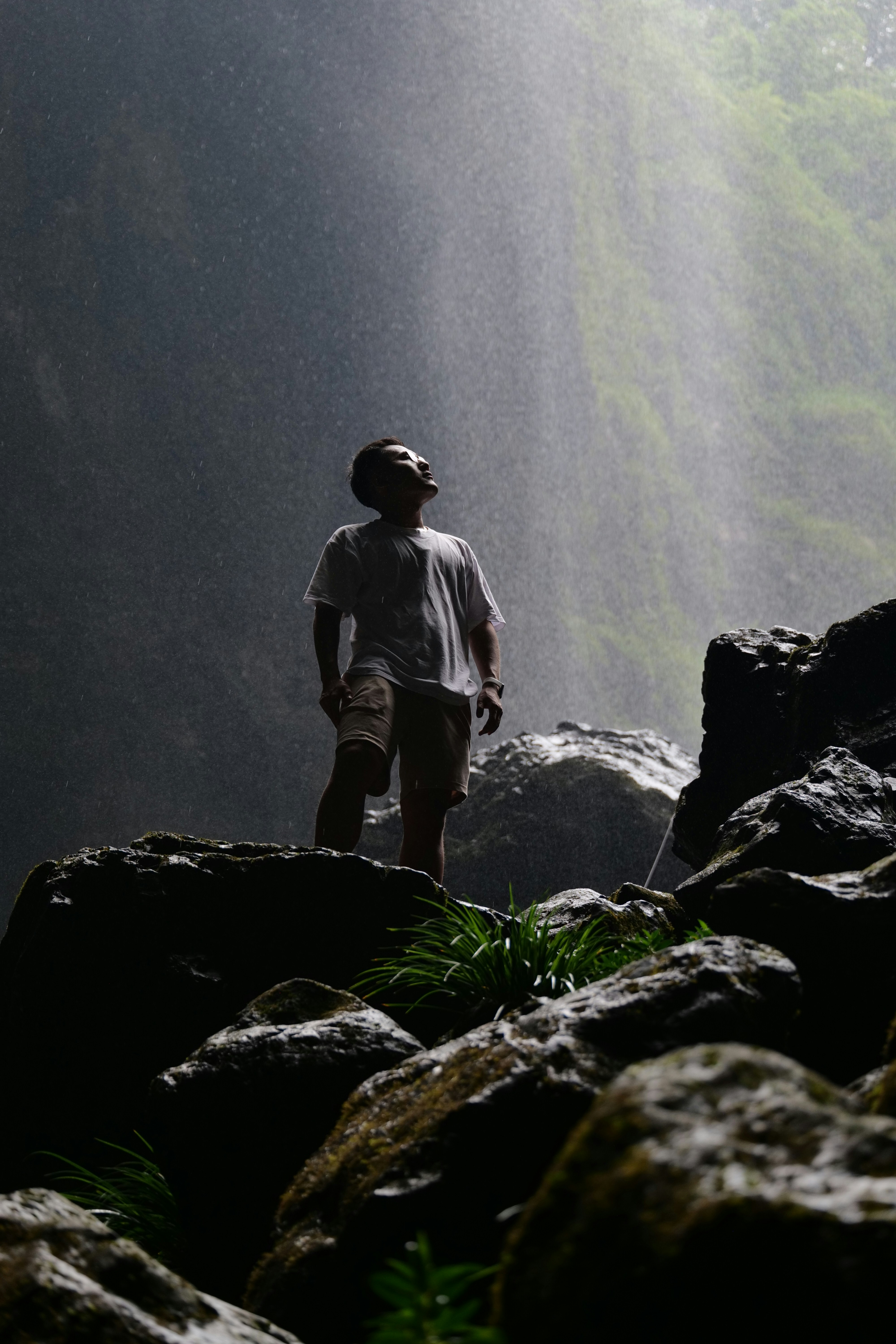 Man standing near a waterfall looking up.