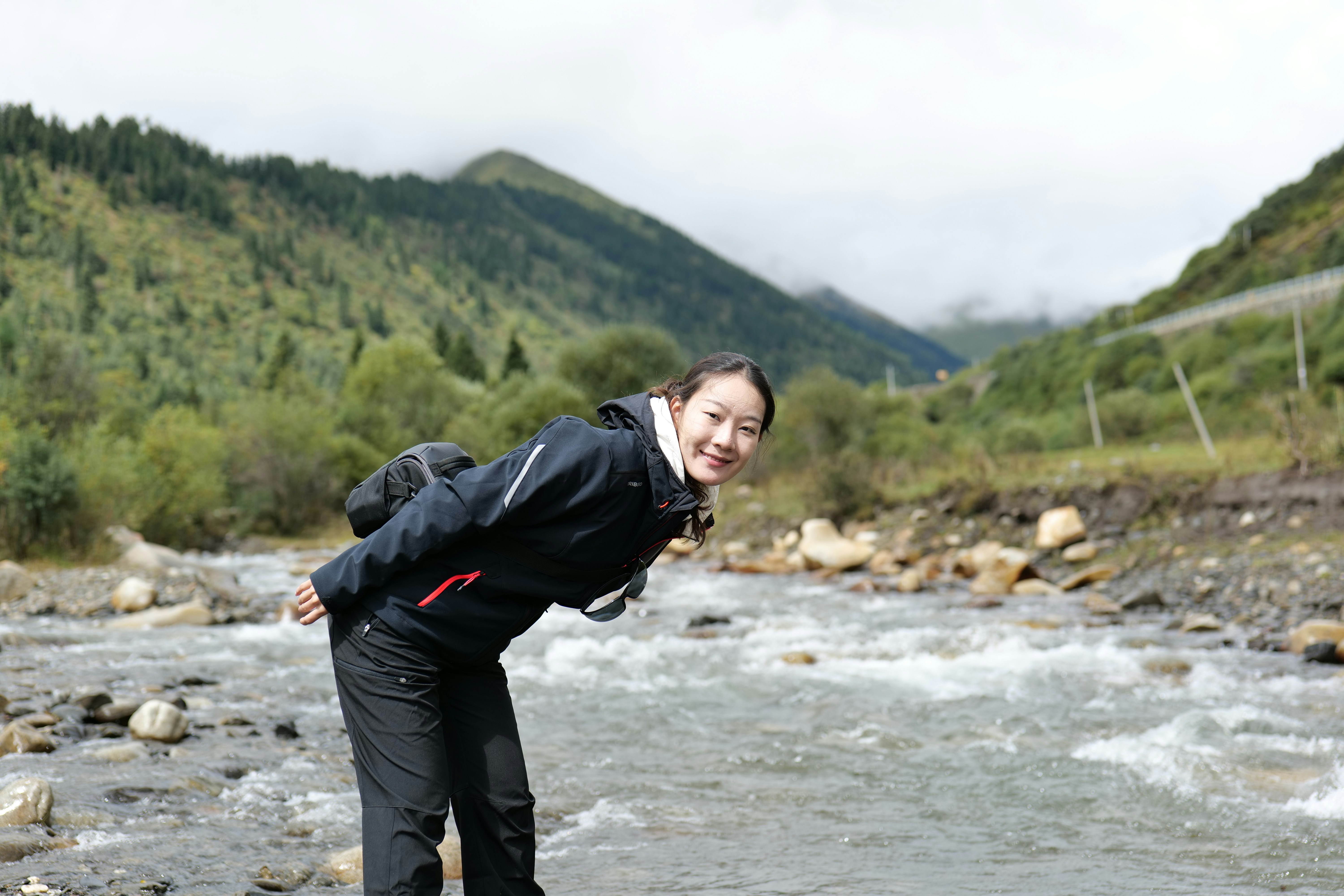 Woman standing by a rocky river with mountains behind