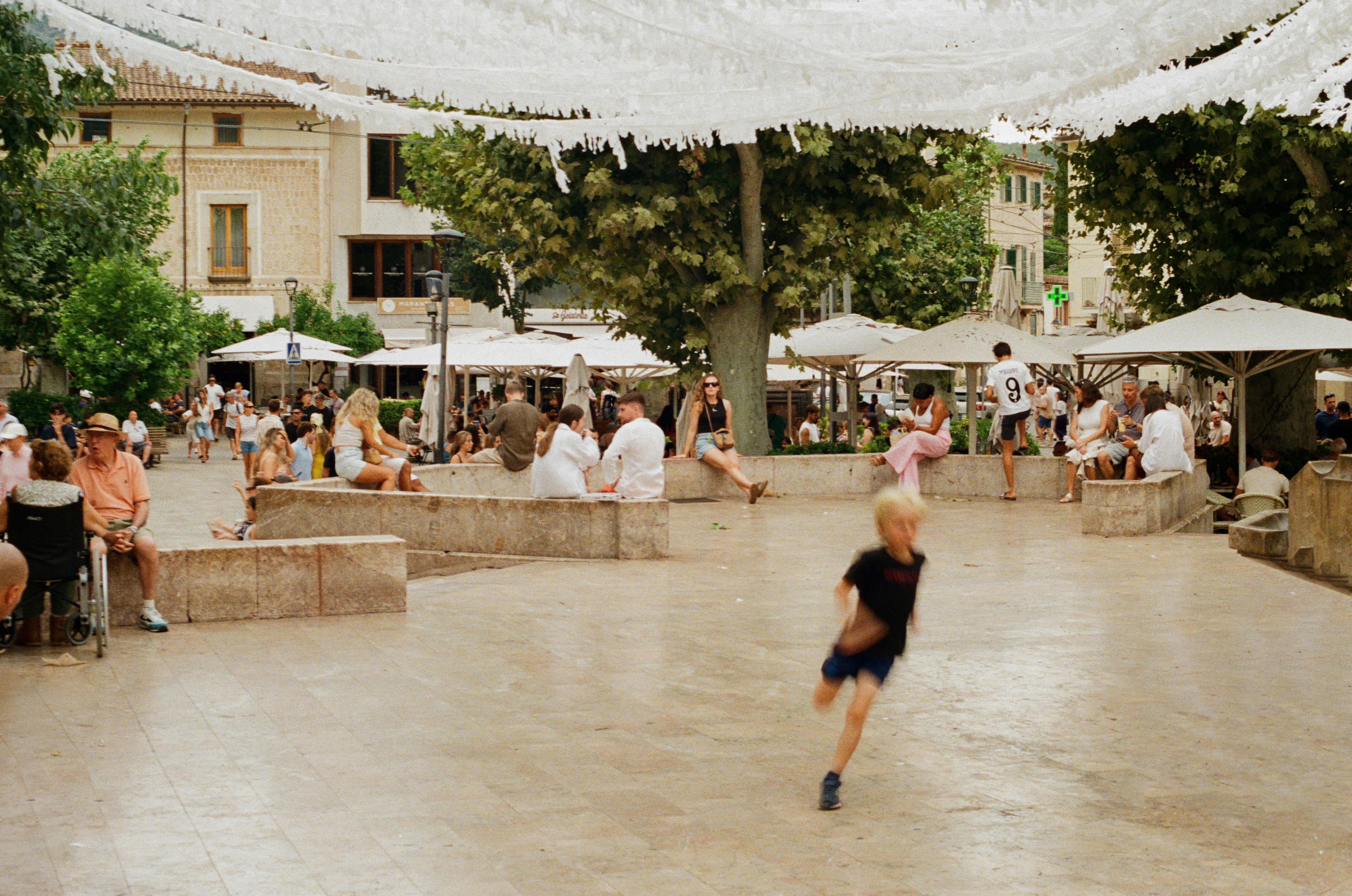 Children play in a sunlit town square with outdoor seating.
