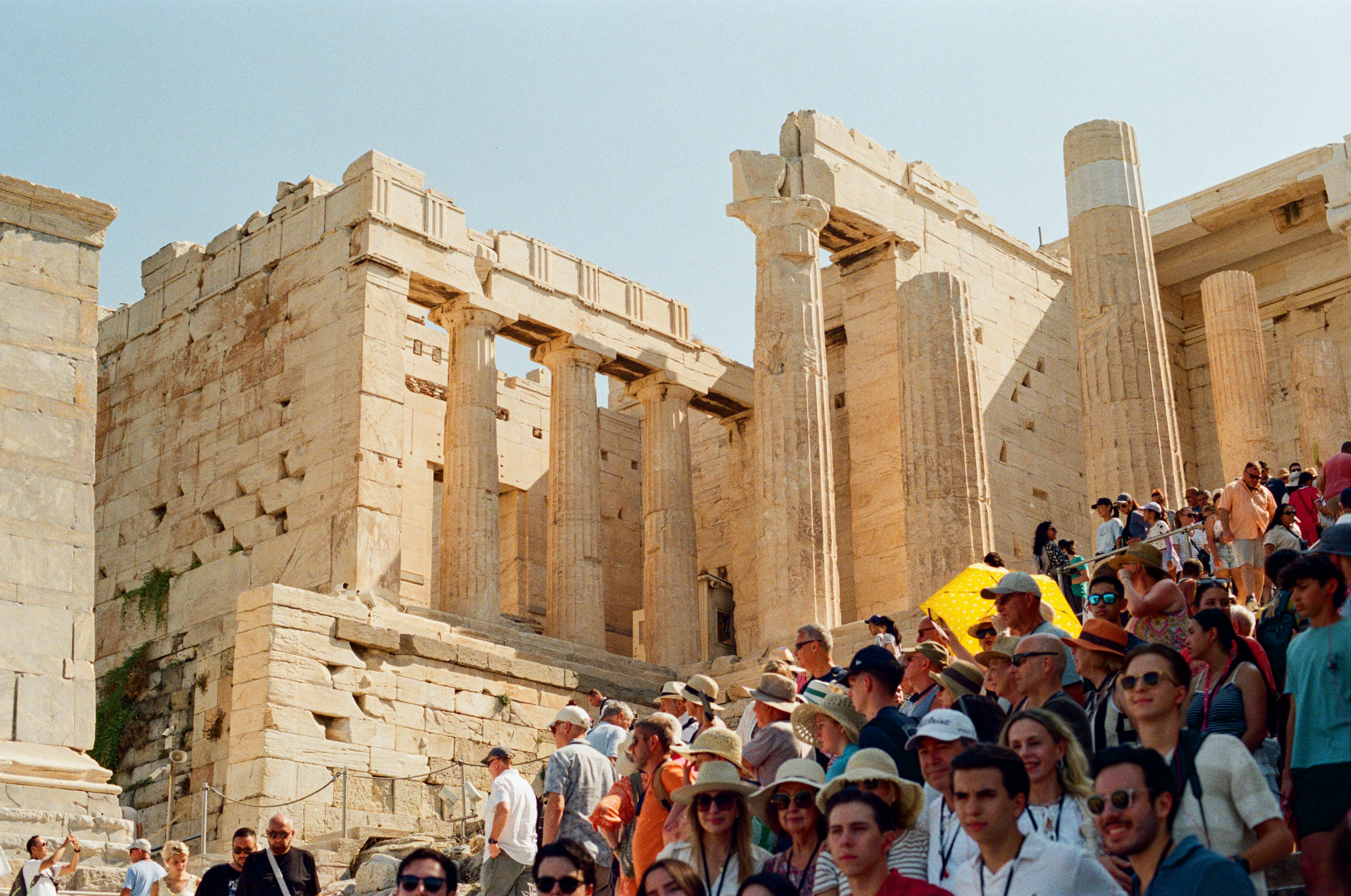 Tourists visit ancient greek ruins under a clear sky.