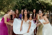 Bride laughing with bridesmaids holding her dress outdoors