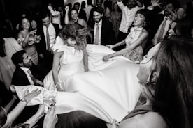 People lifting bride in the air at a celebration.