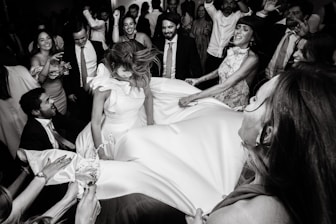 People lifting bride in the air at a celebration.