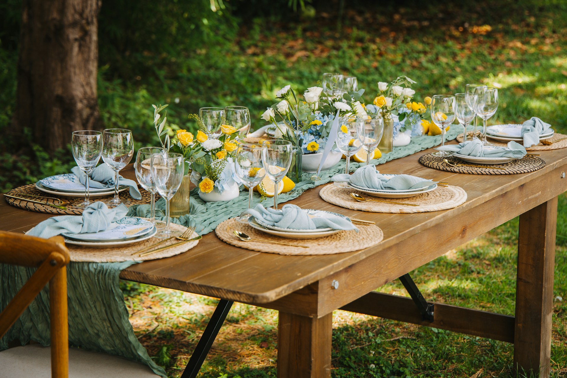 Outdoor table setting with light blue napkins and yellow flowers.