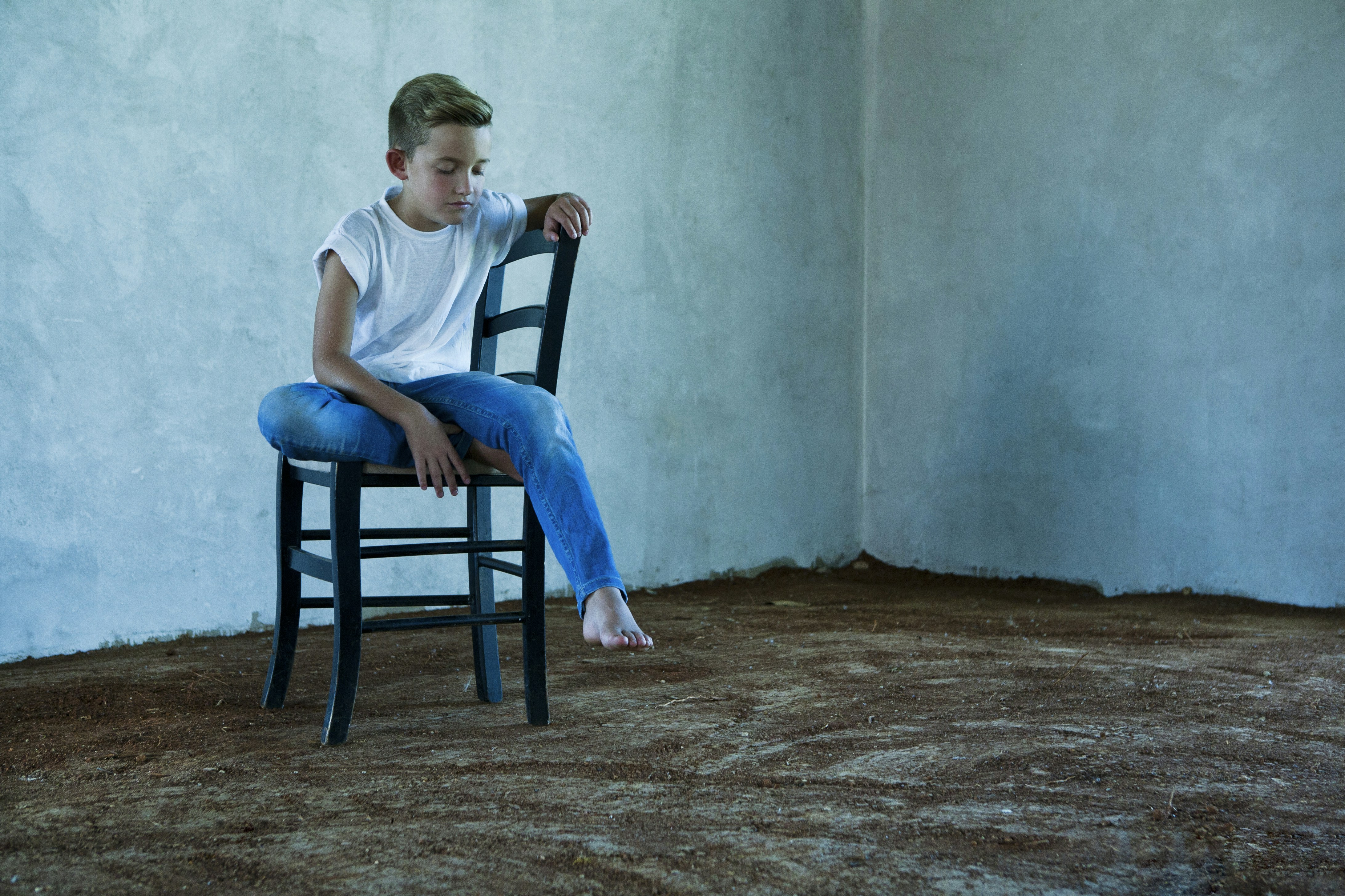 Young boy sitting on a chair in an empty room.