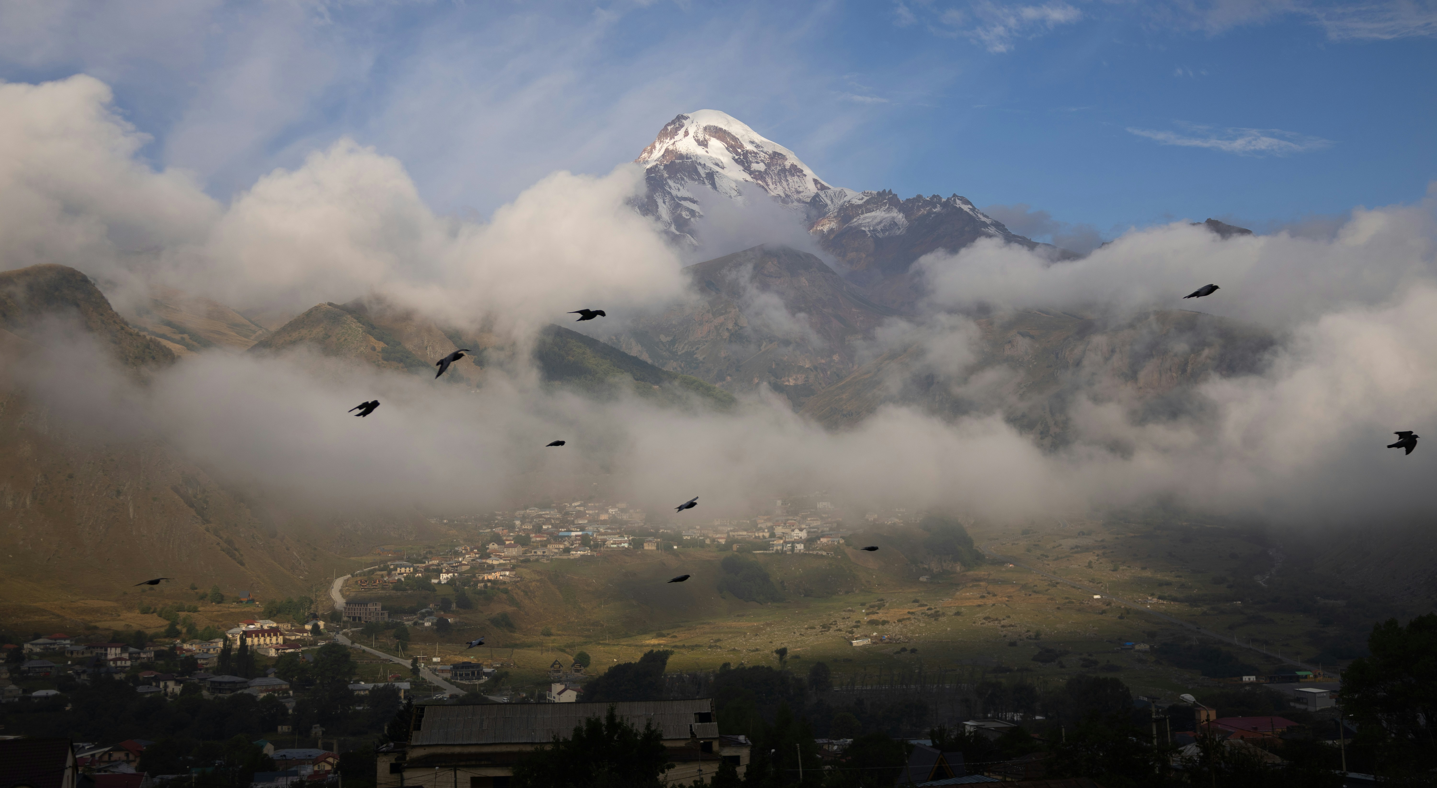 Snow-capped mountain peak emerges from clouds over village.