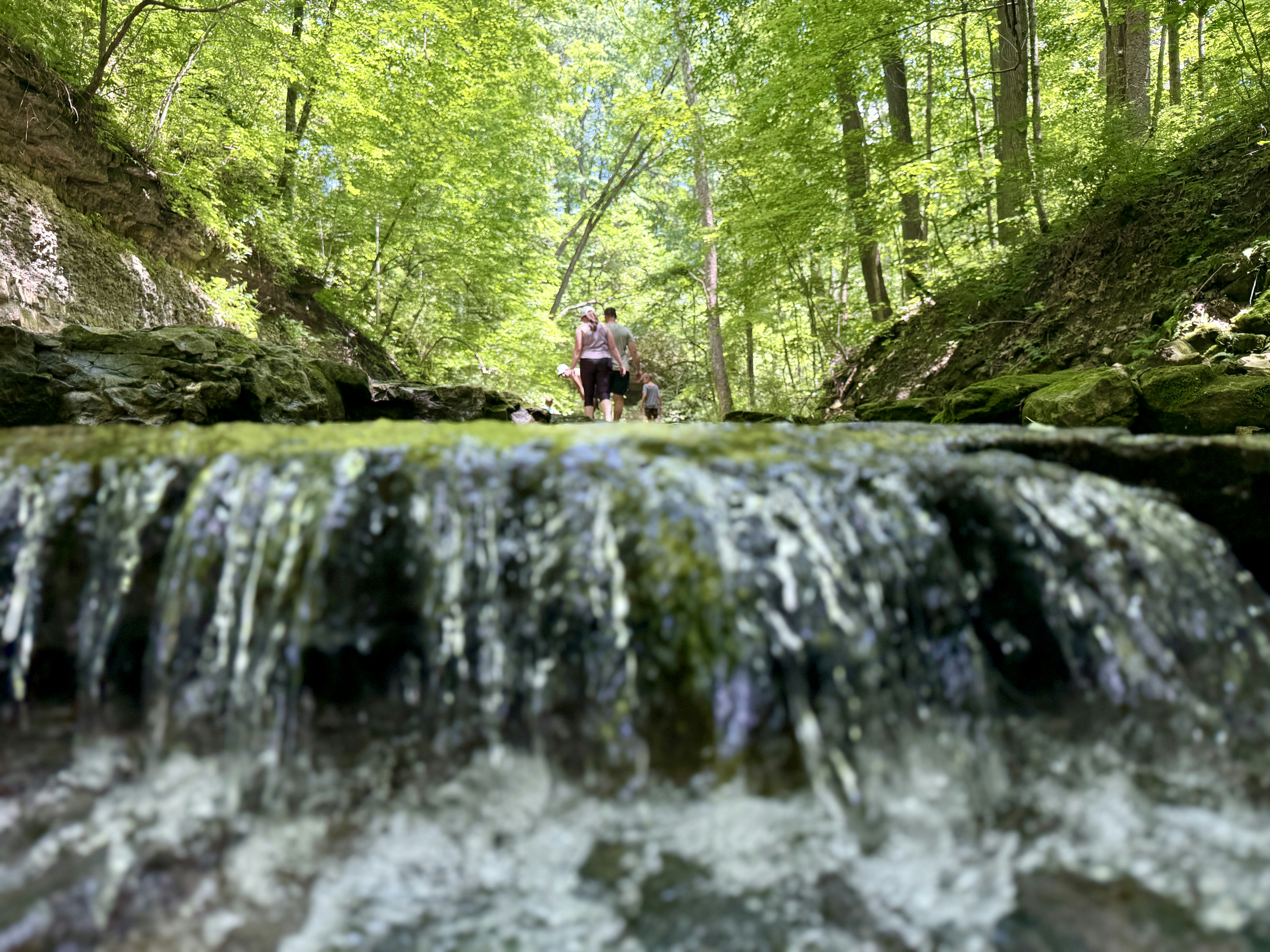 Zwei Personen gehen in der Nähe eines kleinen Wasserfalls in einem Wald spazieren.