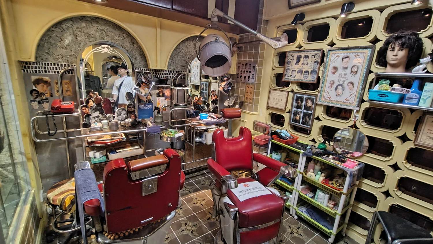 A crowded old barbershop with shelves of bottles behind the chairs