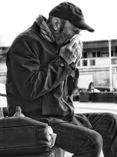 Man sitting outside blowing nose into tissue